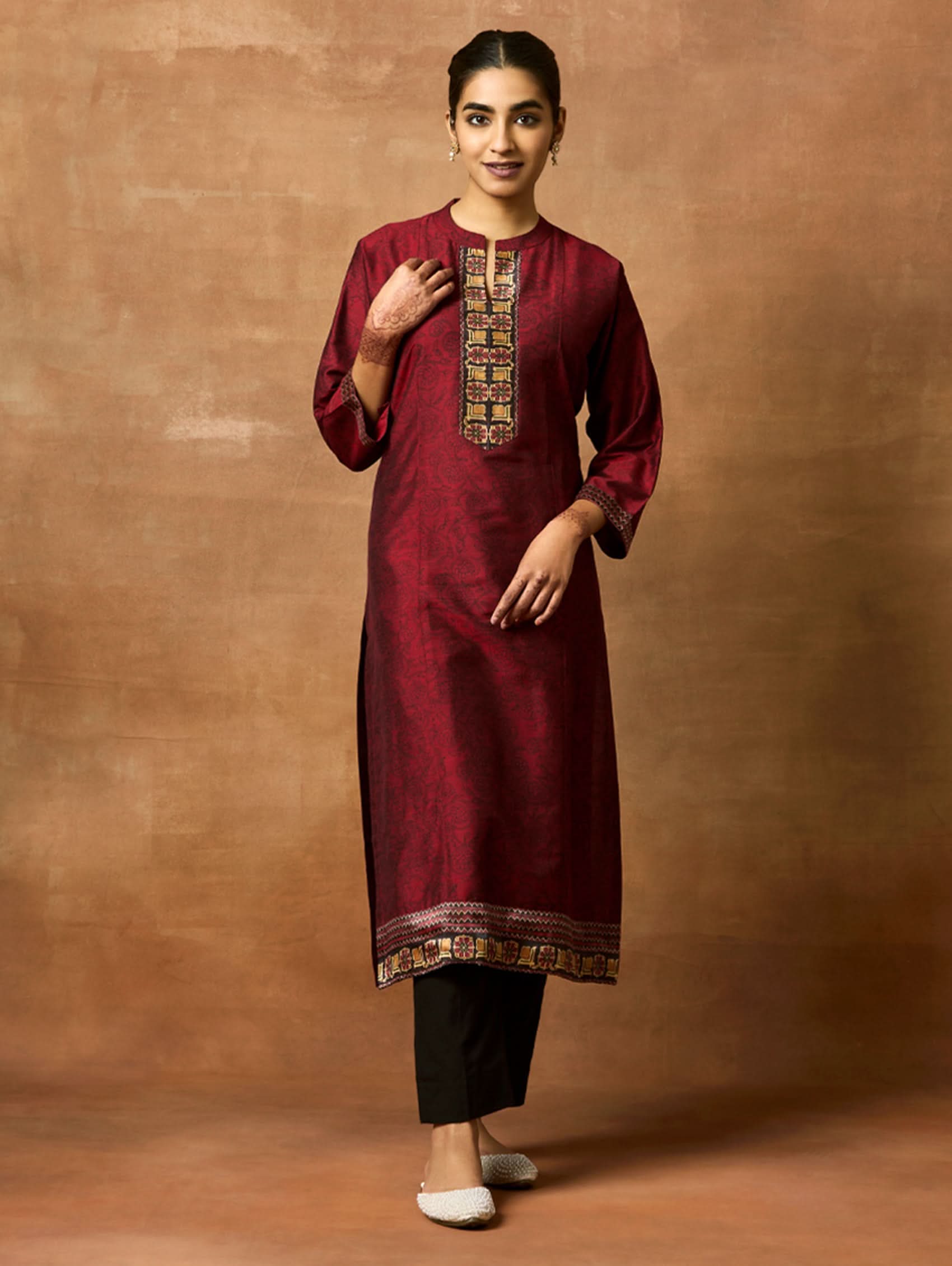 Woman wearing a maroon kurta with black pants against a brown background