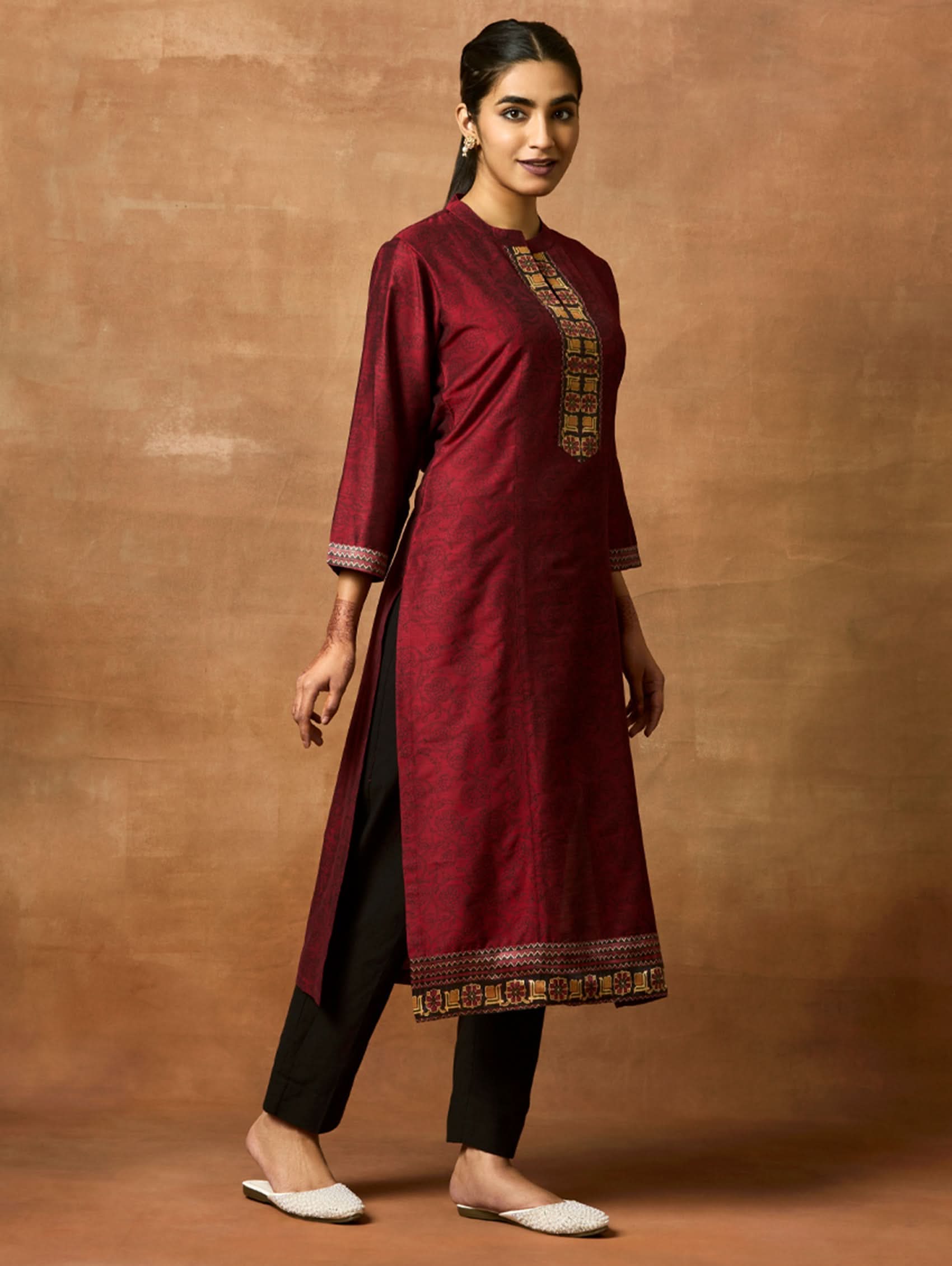 Woman wearing a maroon kurta with gold embroidery on a brown background