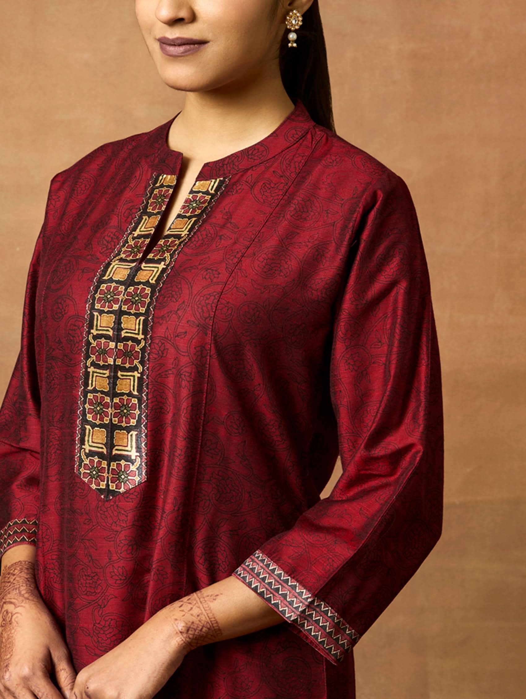 Woman wearing a maroon traditional outfit with intricate patterns on a brown background