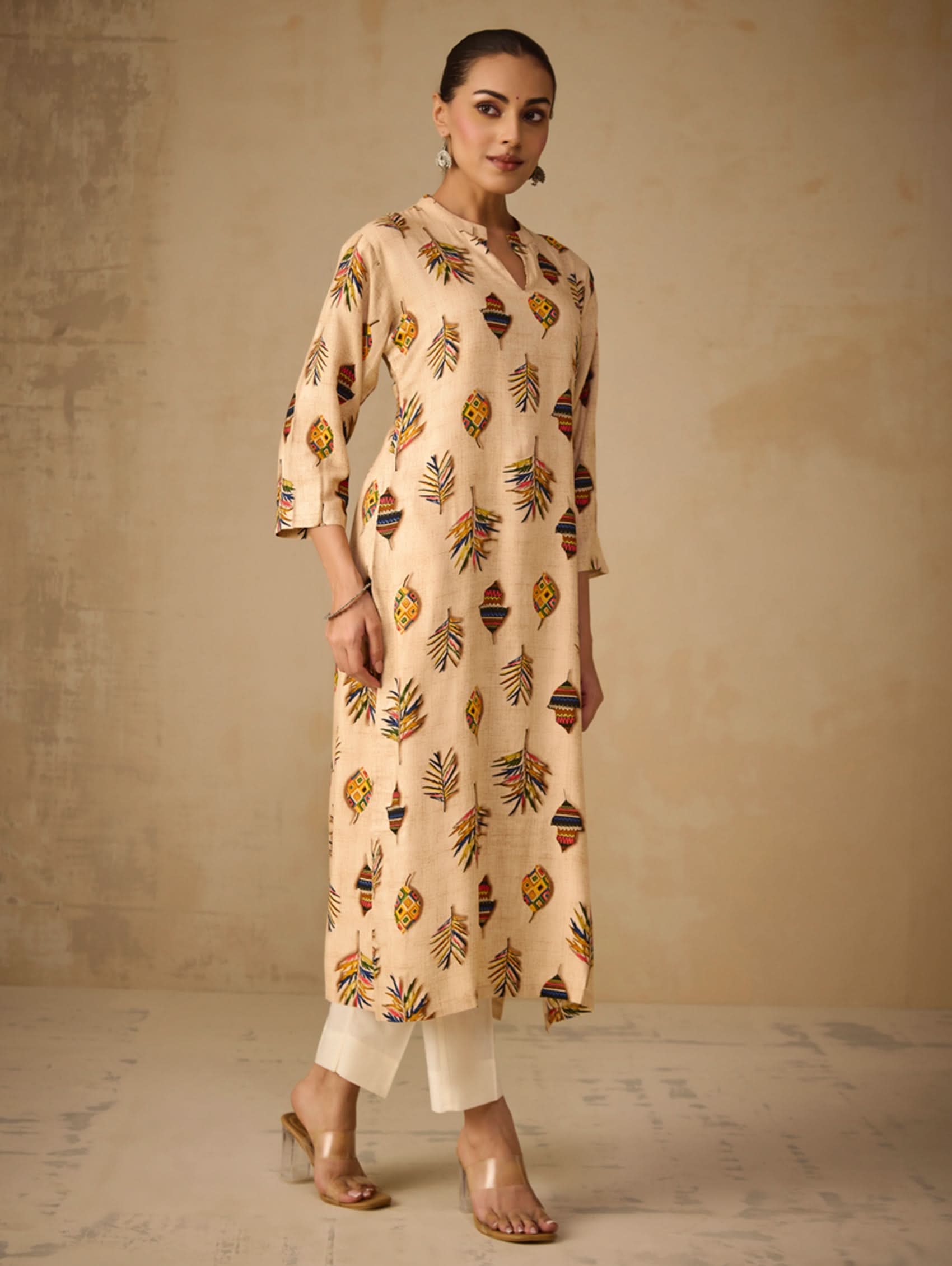 Woman wearing a beige patterned kurta with white pants against a neutral background