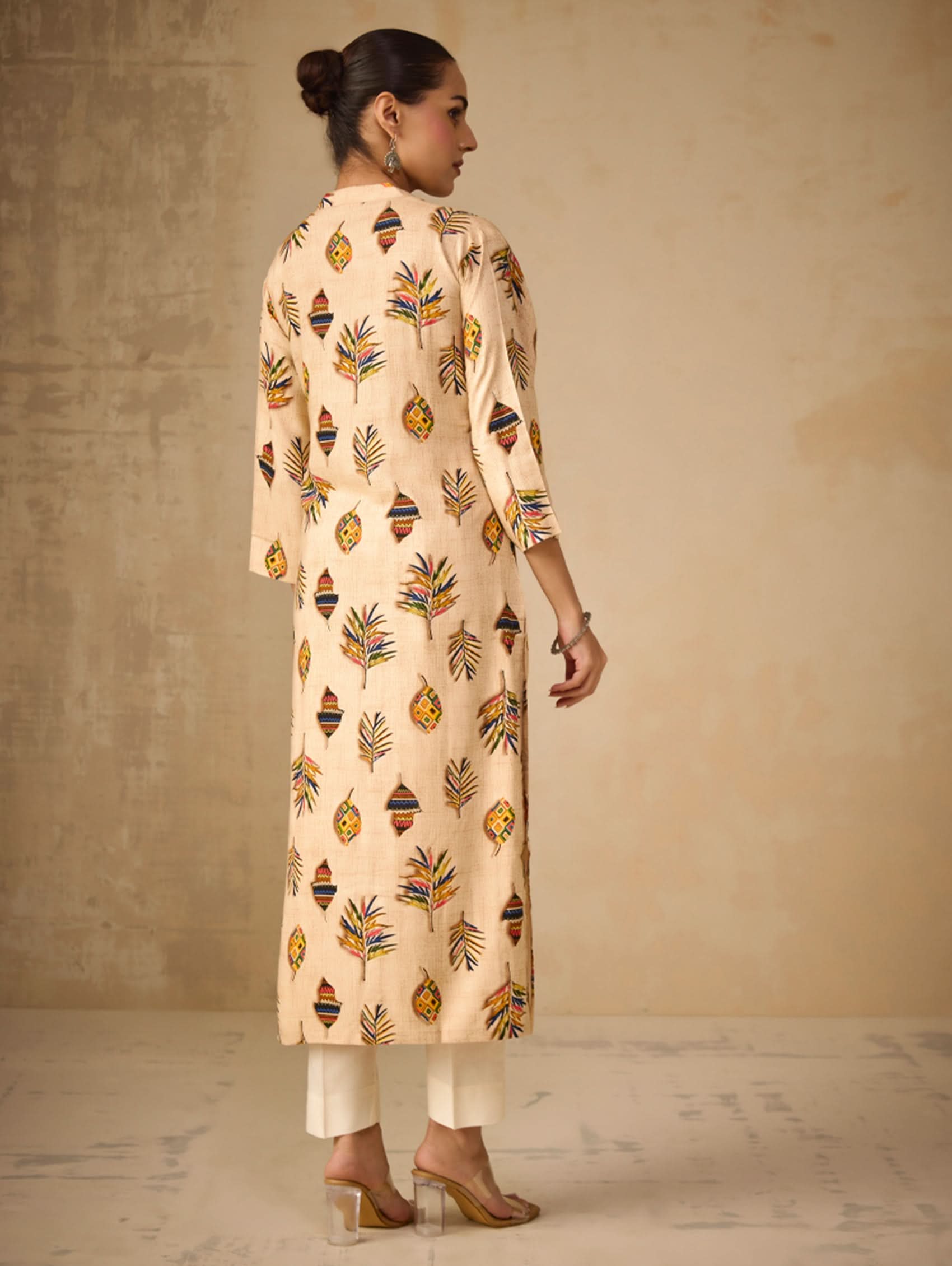Woman wearing a beige kurta with colorful patterns against a plain background