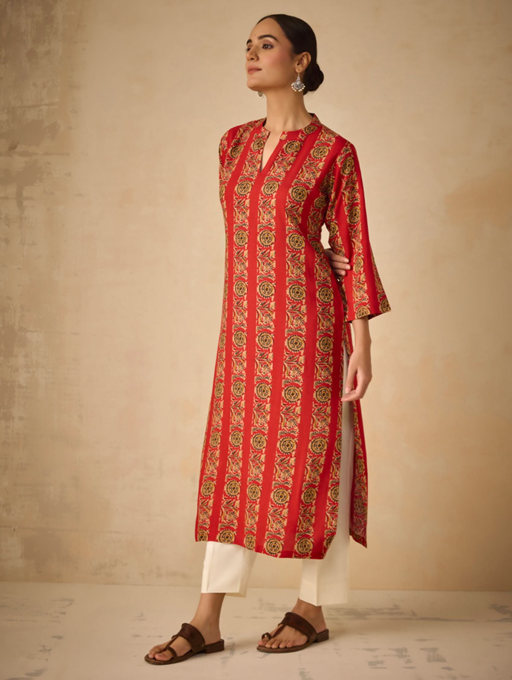 Woman wearing a red patterned kurta with white pants against a beige background