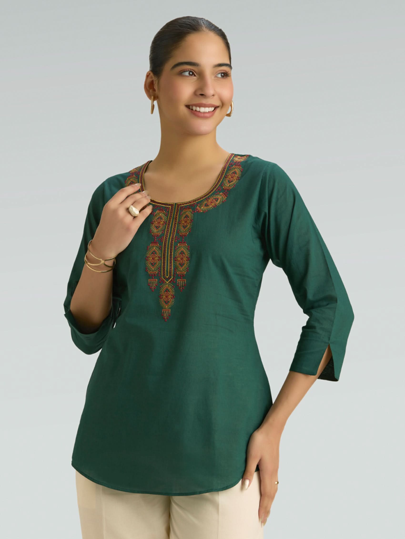 Woman wearing a green embroidered top against a plain background