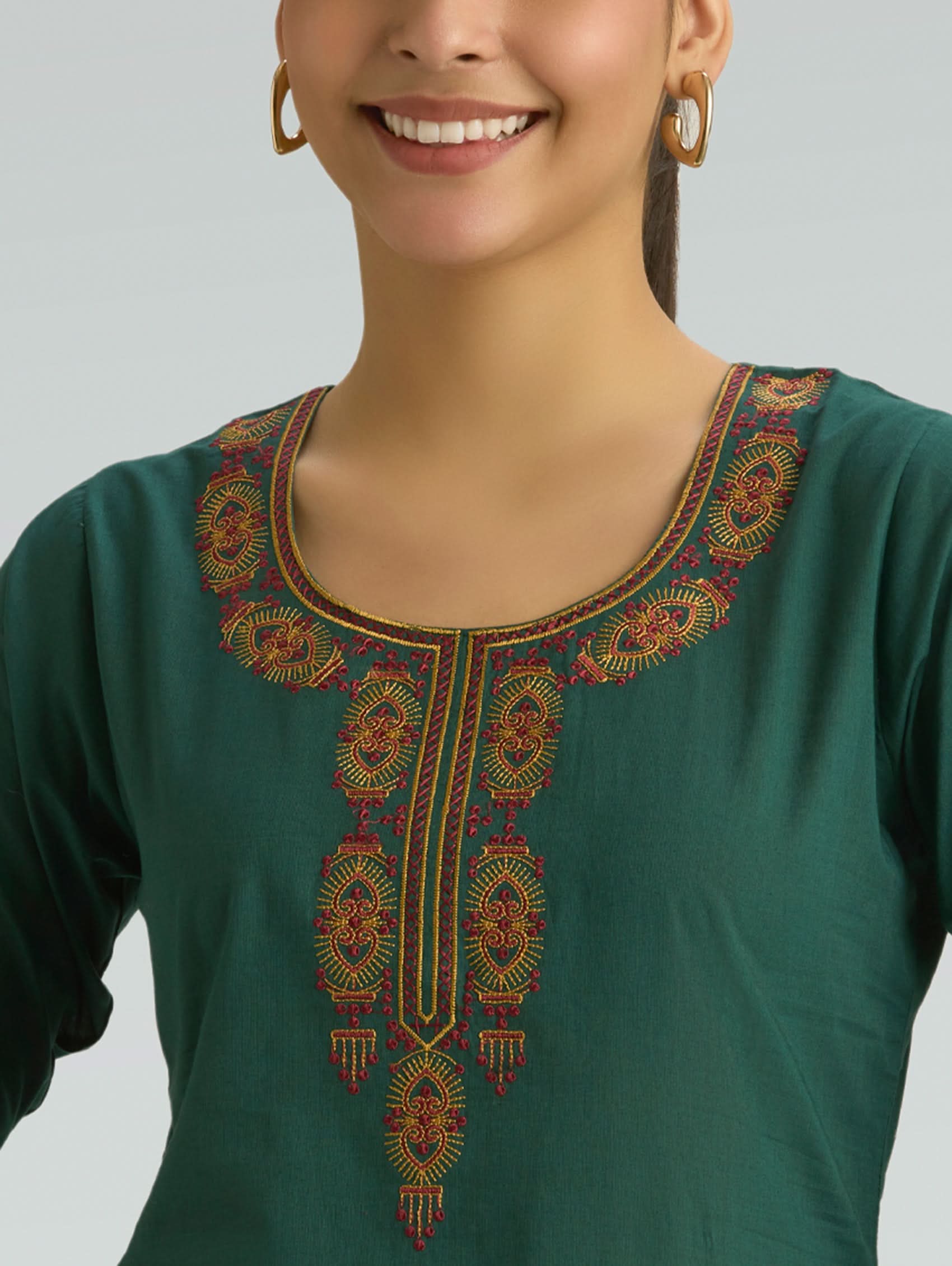 Woman wearing a green top with intricate embroidery on a plain background