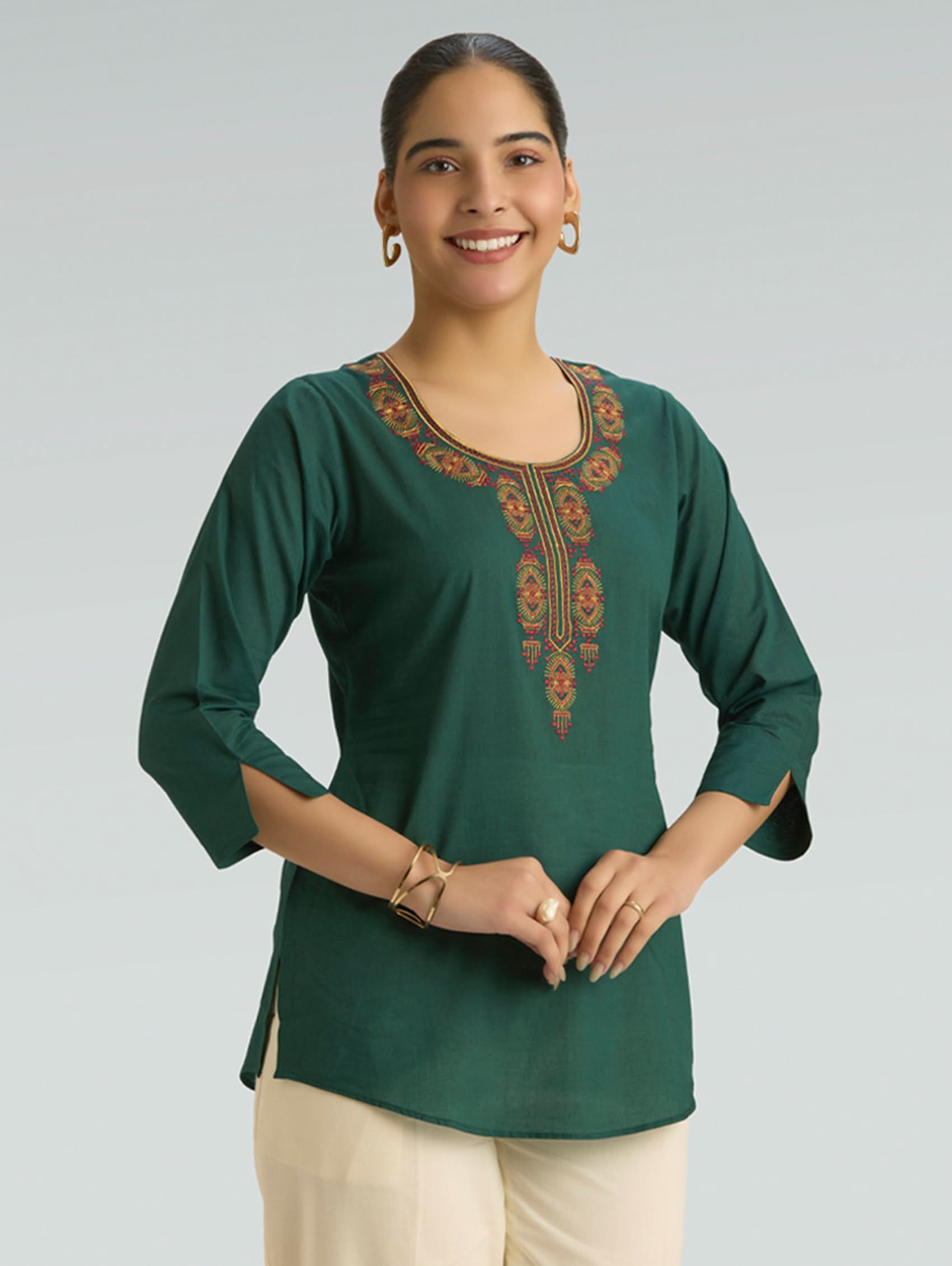 Woman wearing a green embroidered top against a gray background
