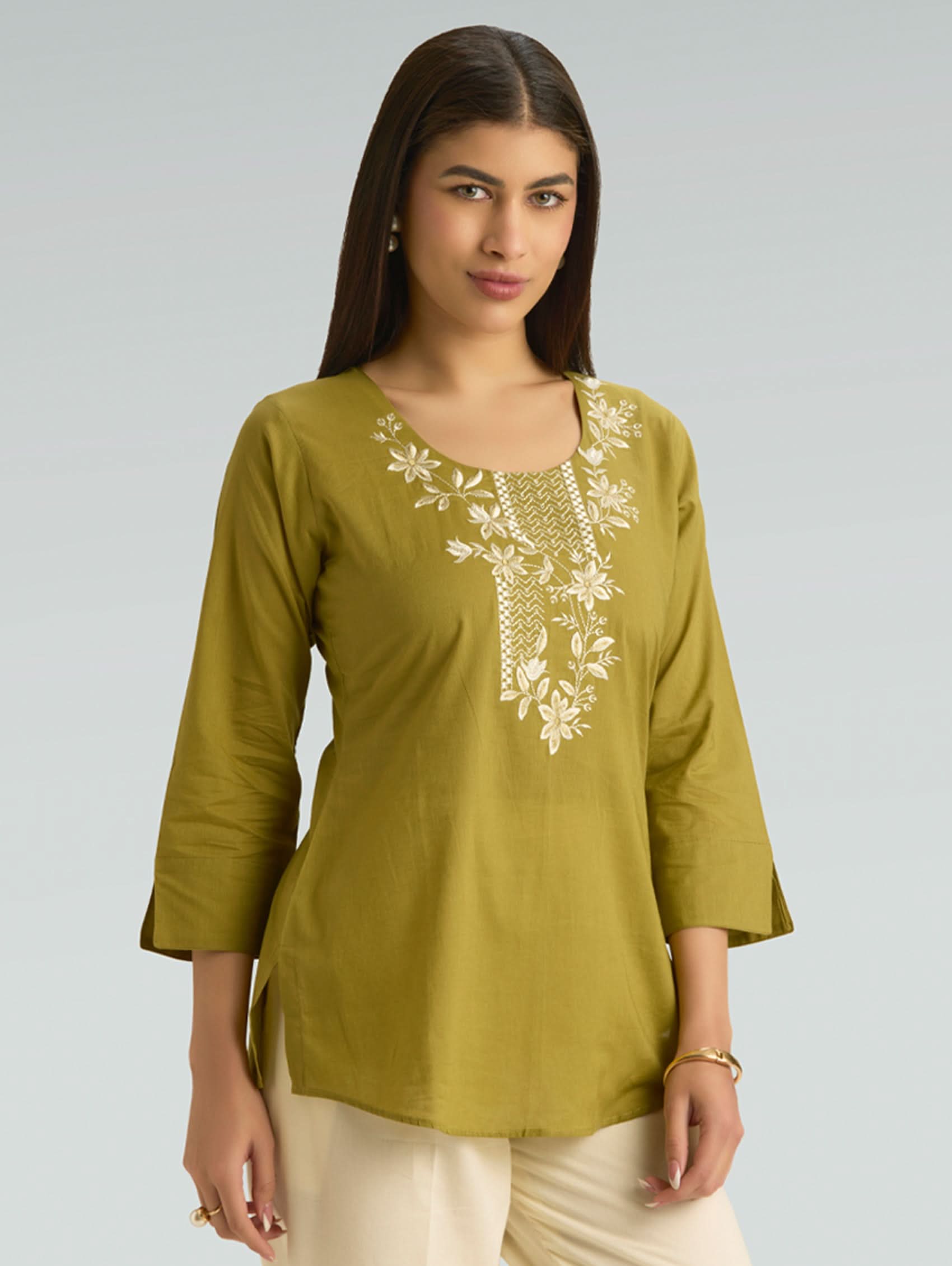 Woman wearing a green embroidered top against a gray background
