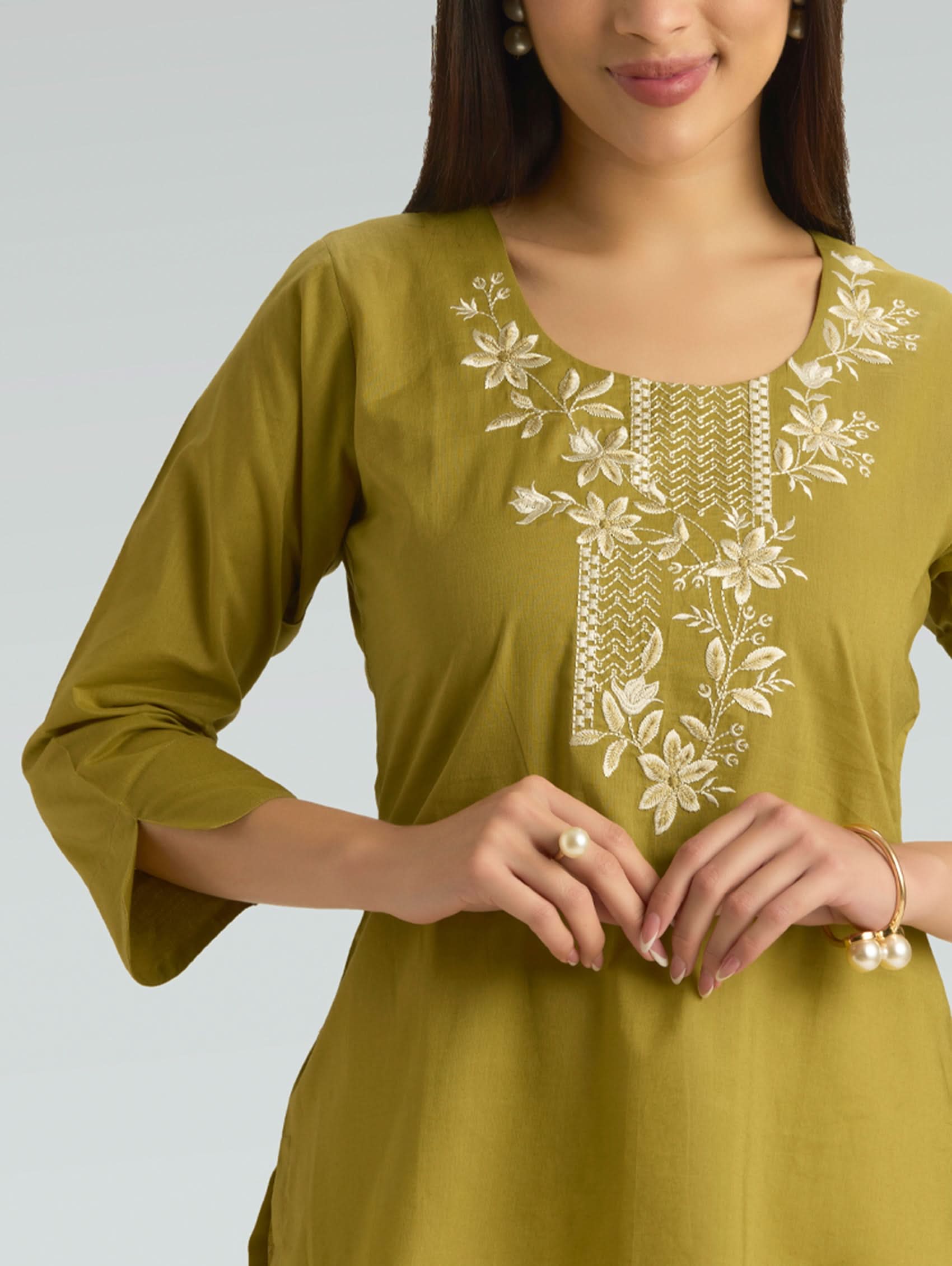 Woman wearing a green kurta with white floral embroidery on a plain background