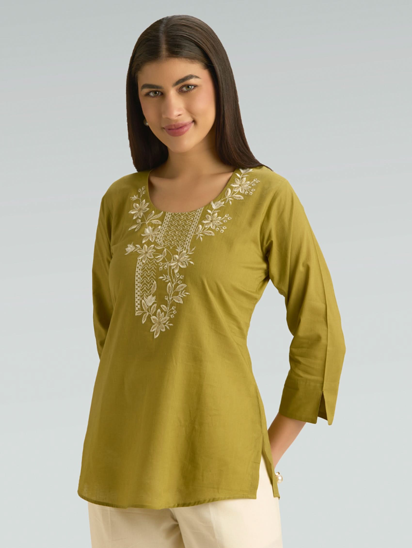 Woman wearing a green embroidered top against a gray background
