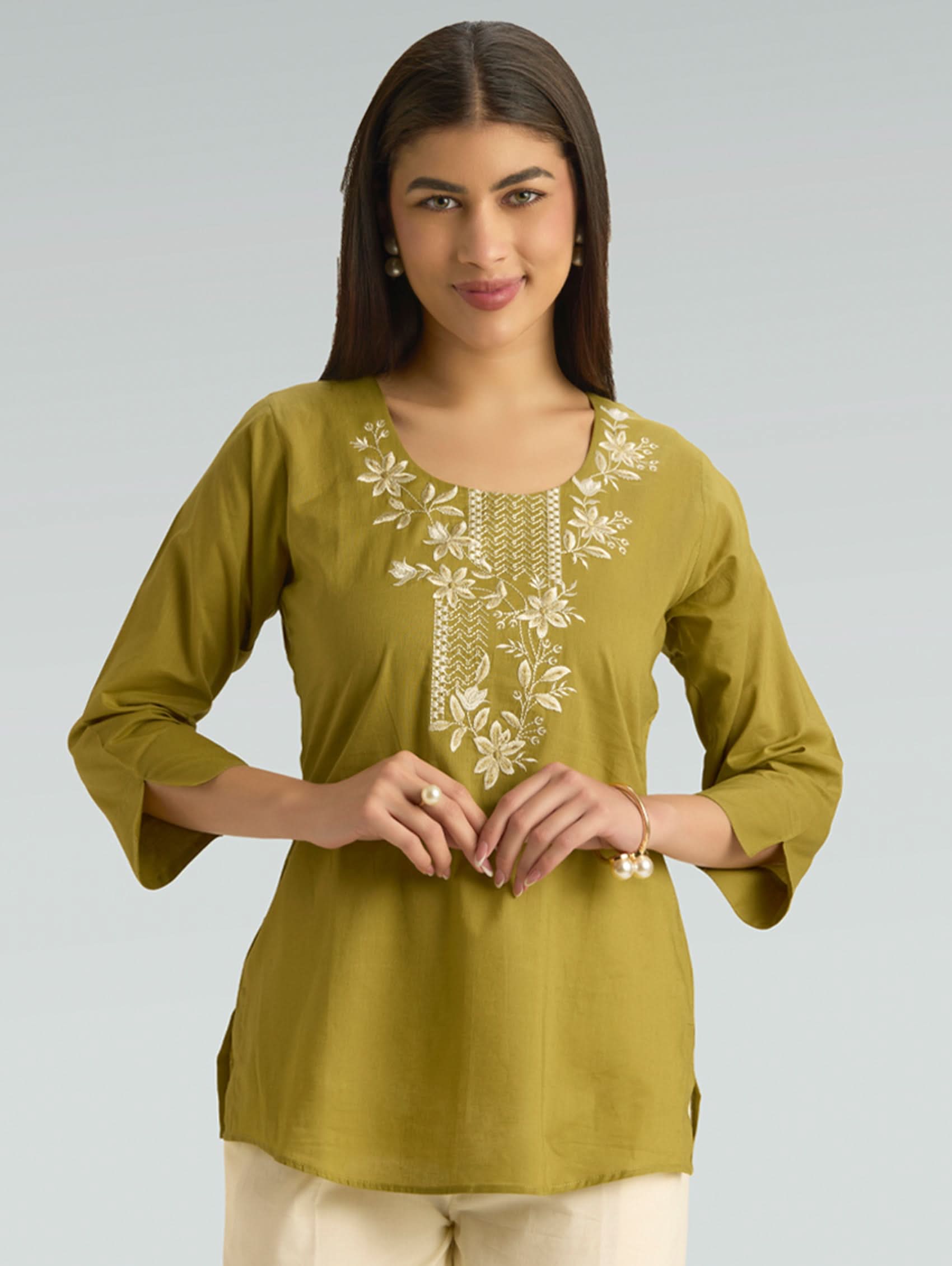 Woman wearing a green embroidered top against a gray background