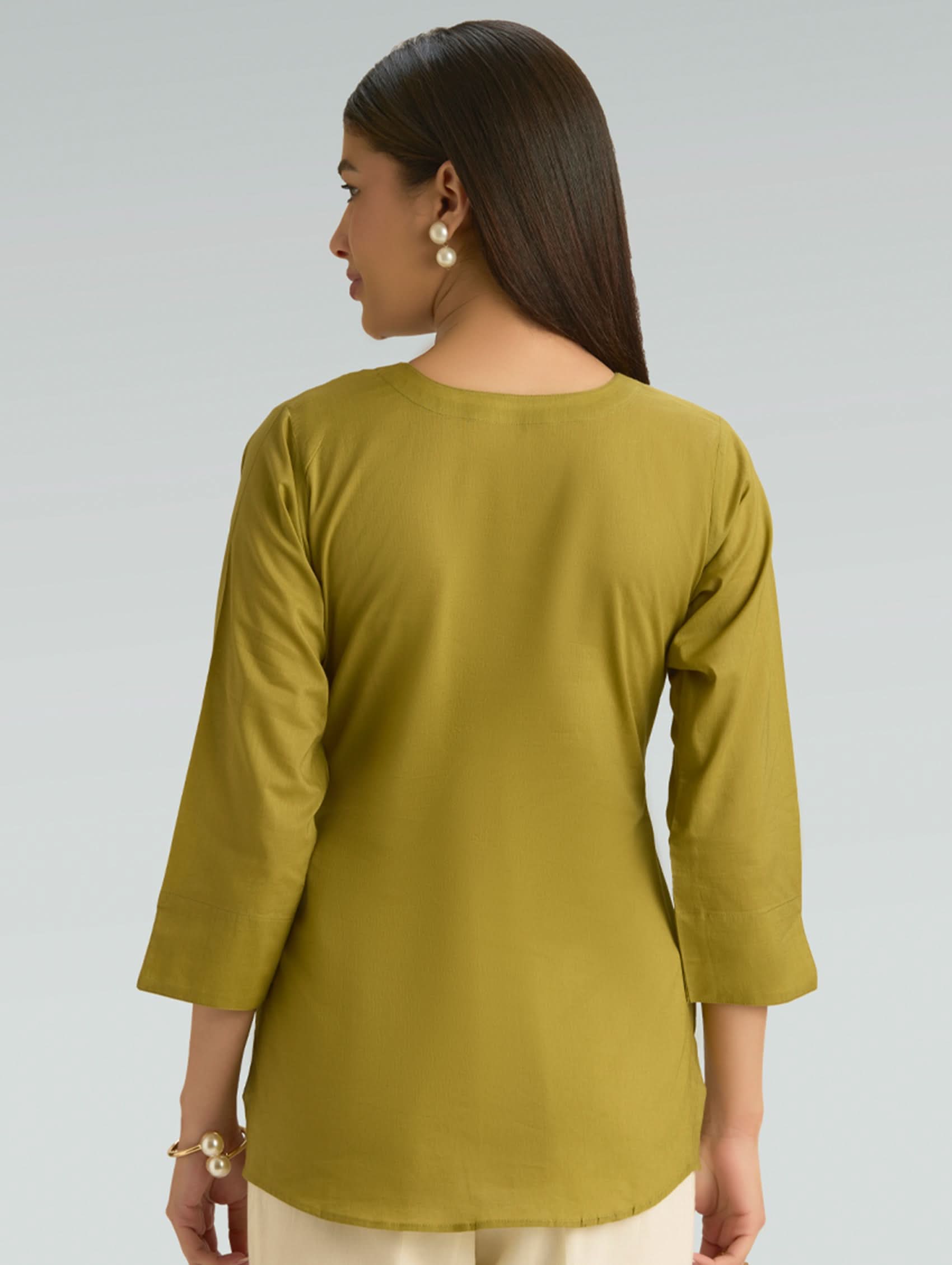 Woman wearing a green long-sleeve top on a gray background