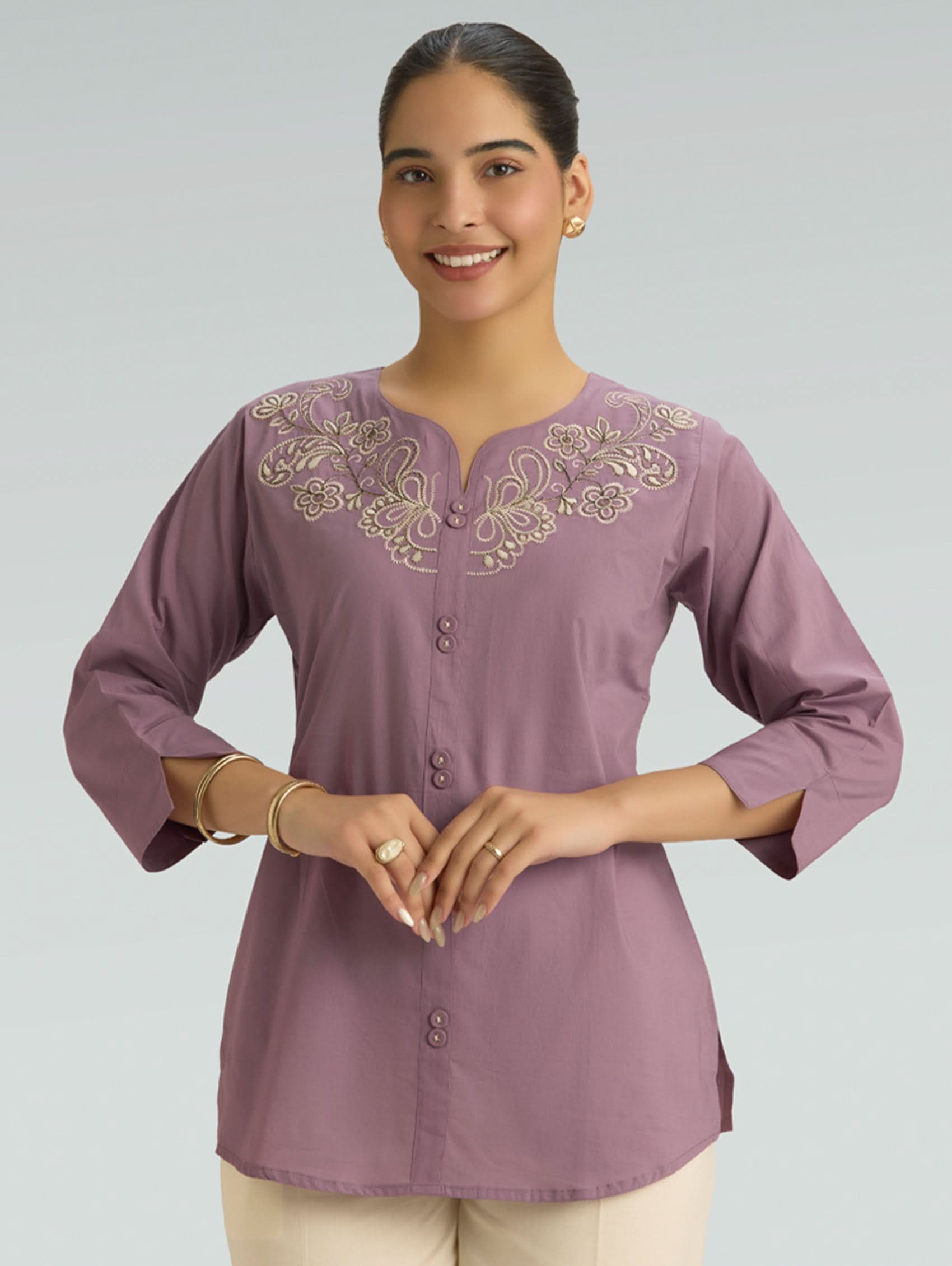 Woman wearing a purple embroidered blouse on a plain background
