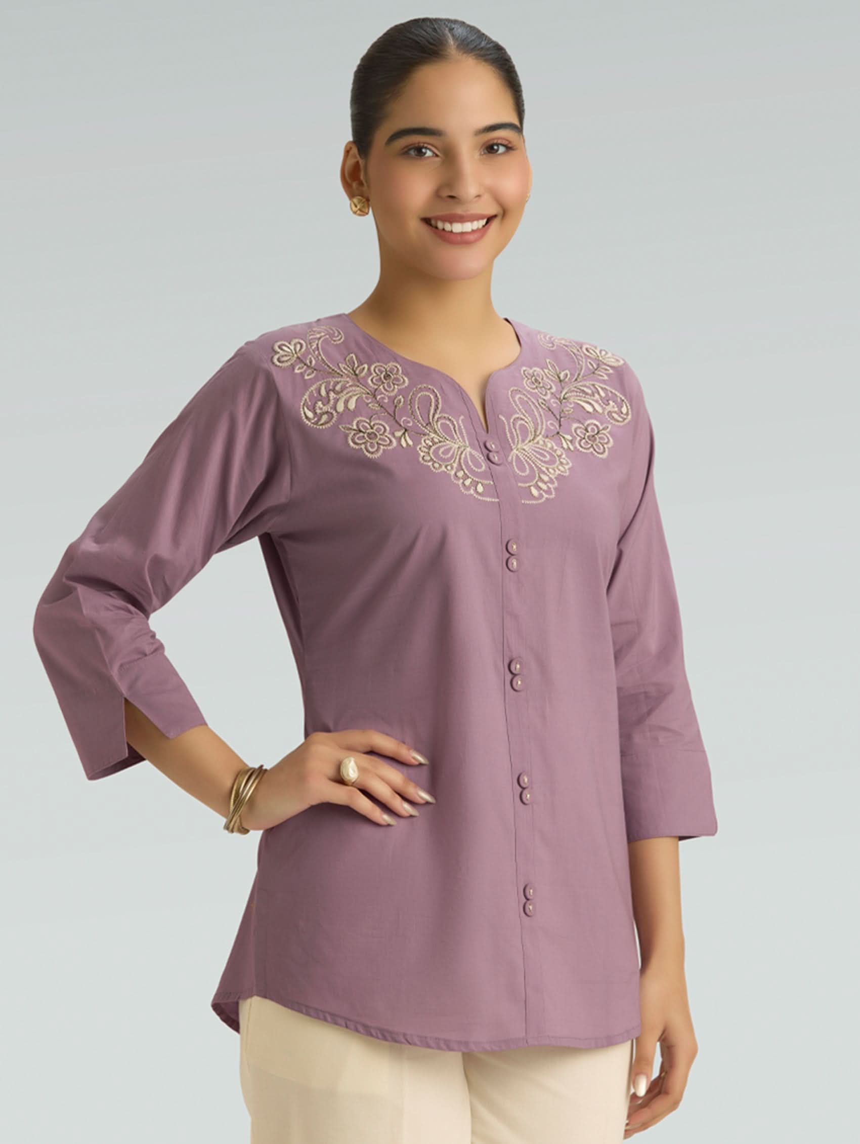 Woman wearing a purple embroidered blouse against a gray background