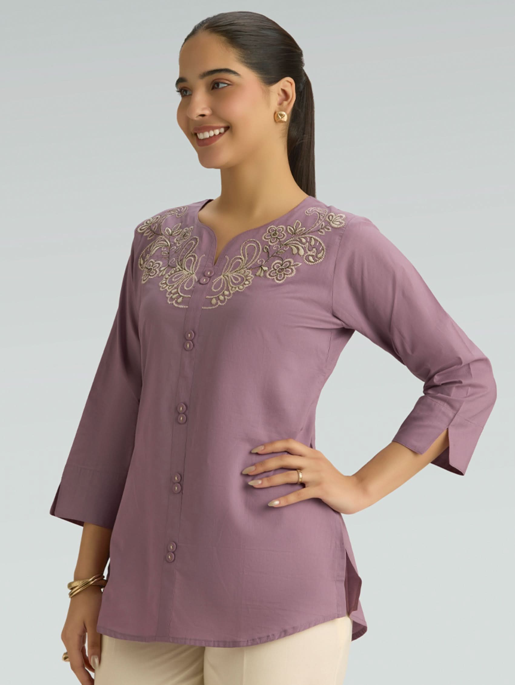 Woman wearing a purple embroidered blouse against a gray background
