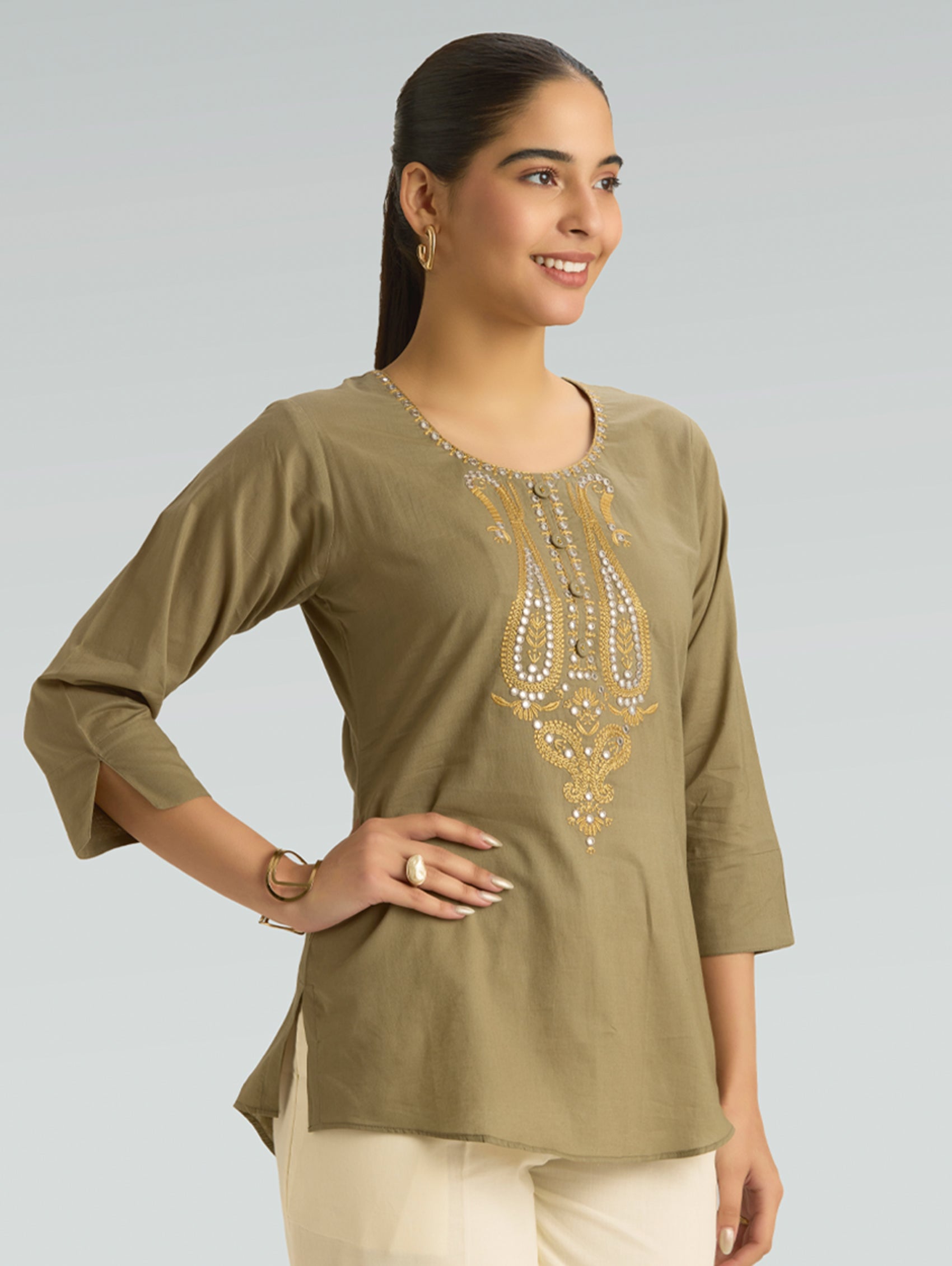 Woman wearing a green embroidered top against a gray background