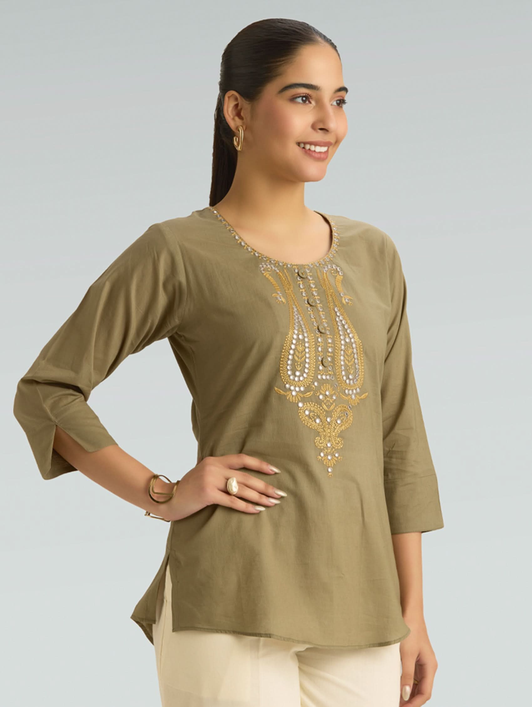 Woman wearing a green embroidered top against a gray background