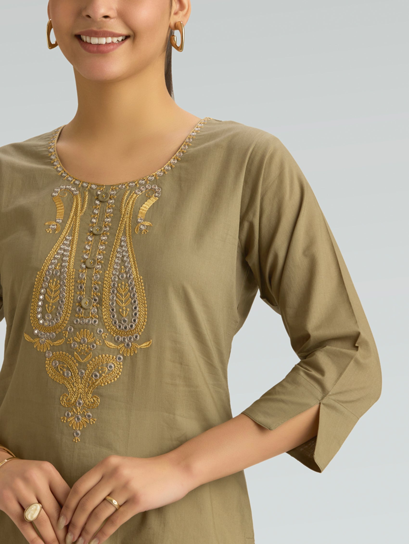 Woman wearing a beige kurta with gold embroidery on a plain background
