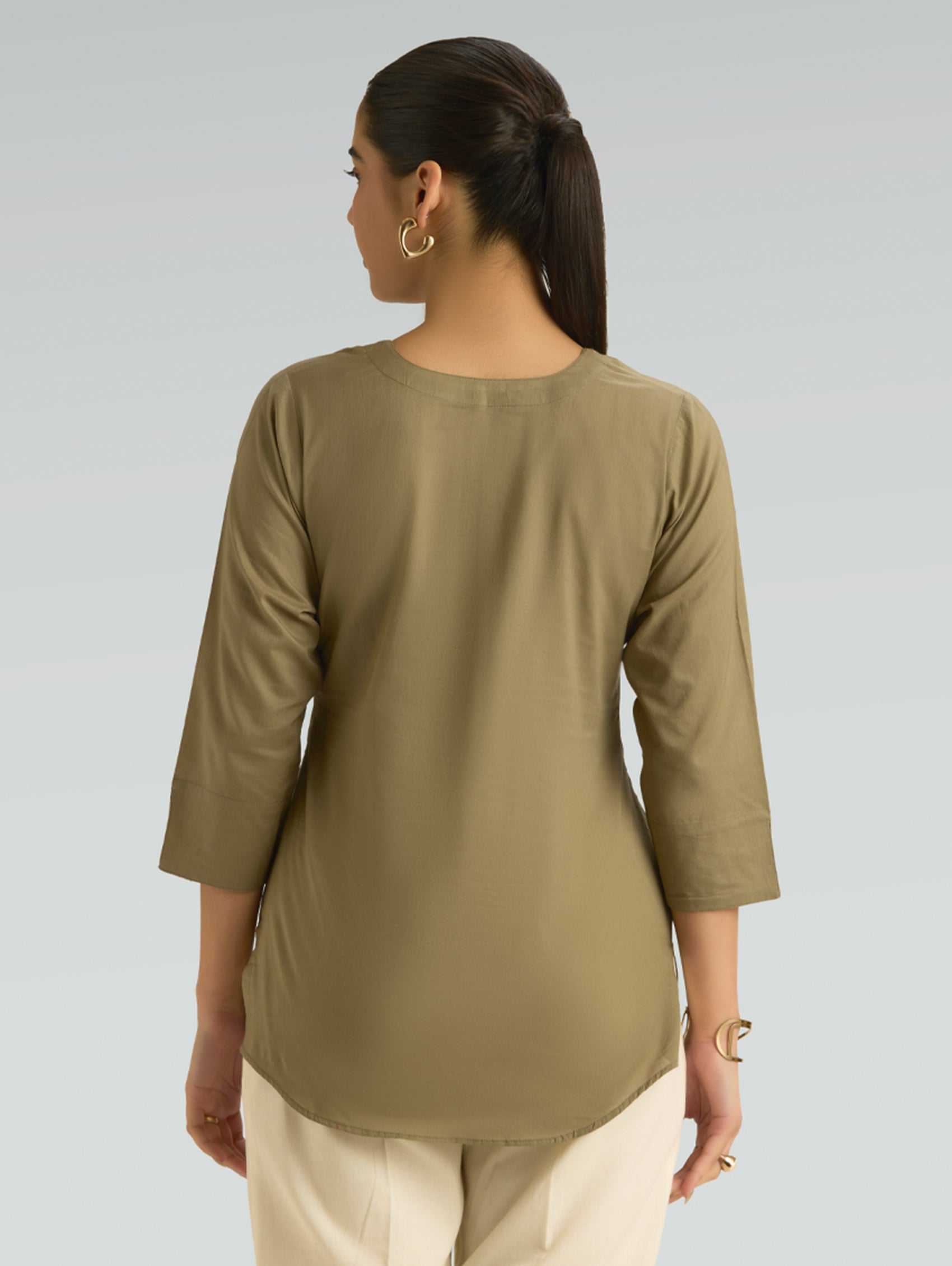 Woman wearing a green long-sleeve top against a gray background