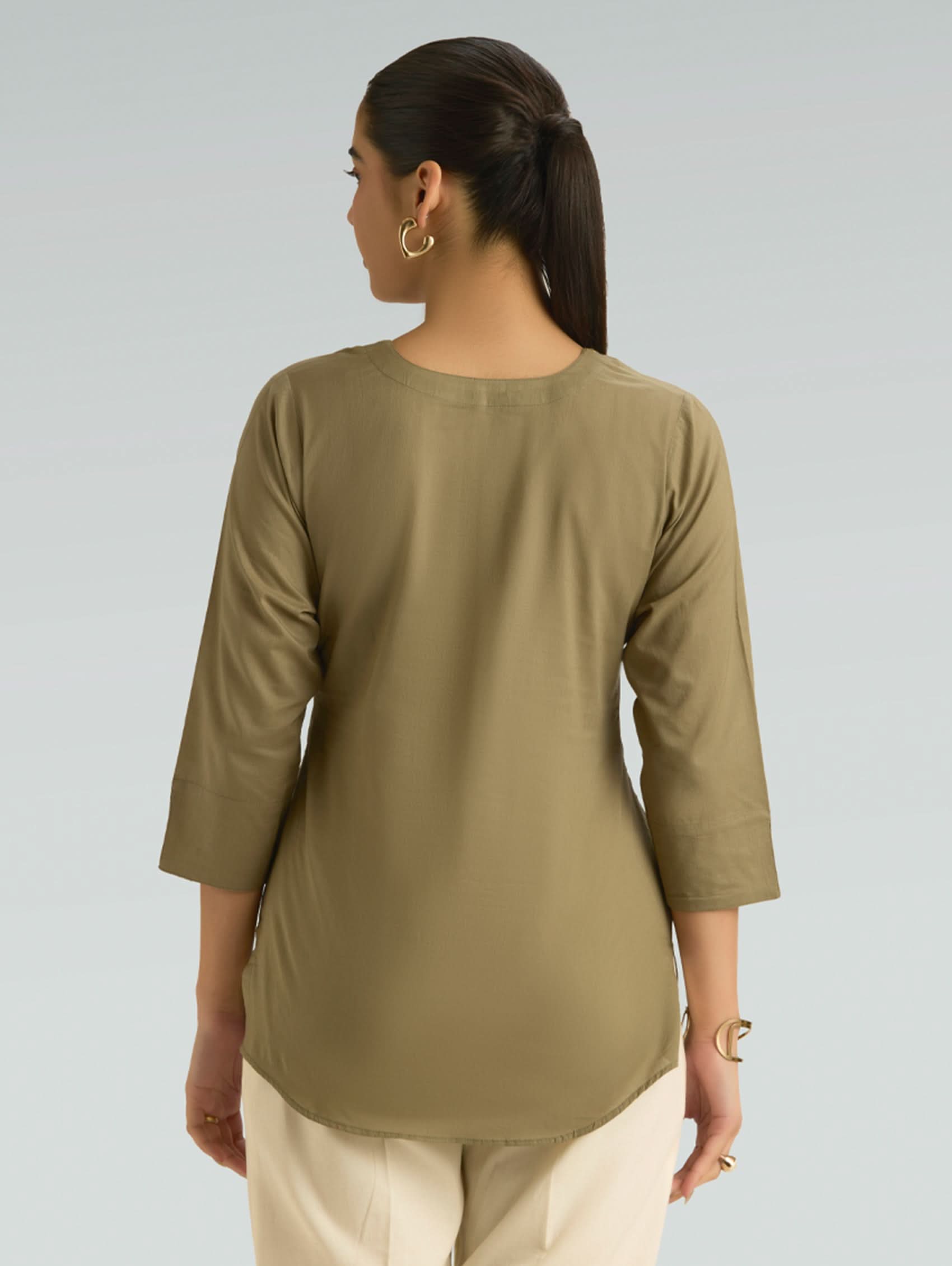 Woman wearing a green long-sleeve top against a gray background
