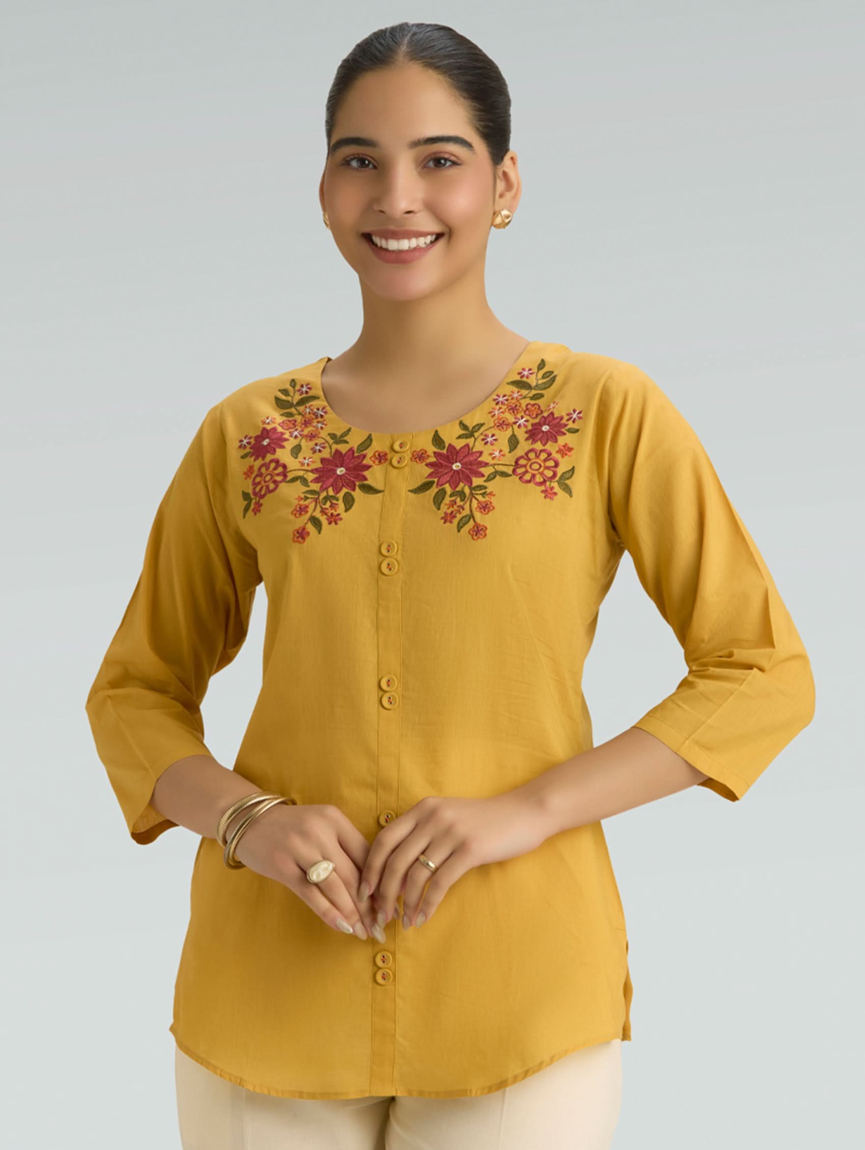 Woman wearing a yellow embroidered top against a plain background