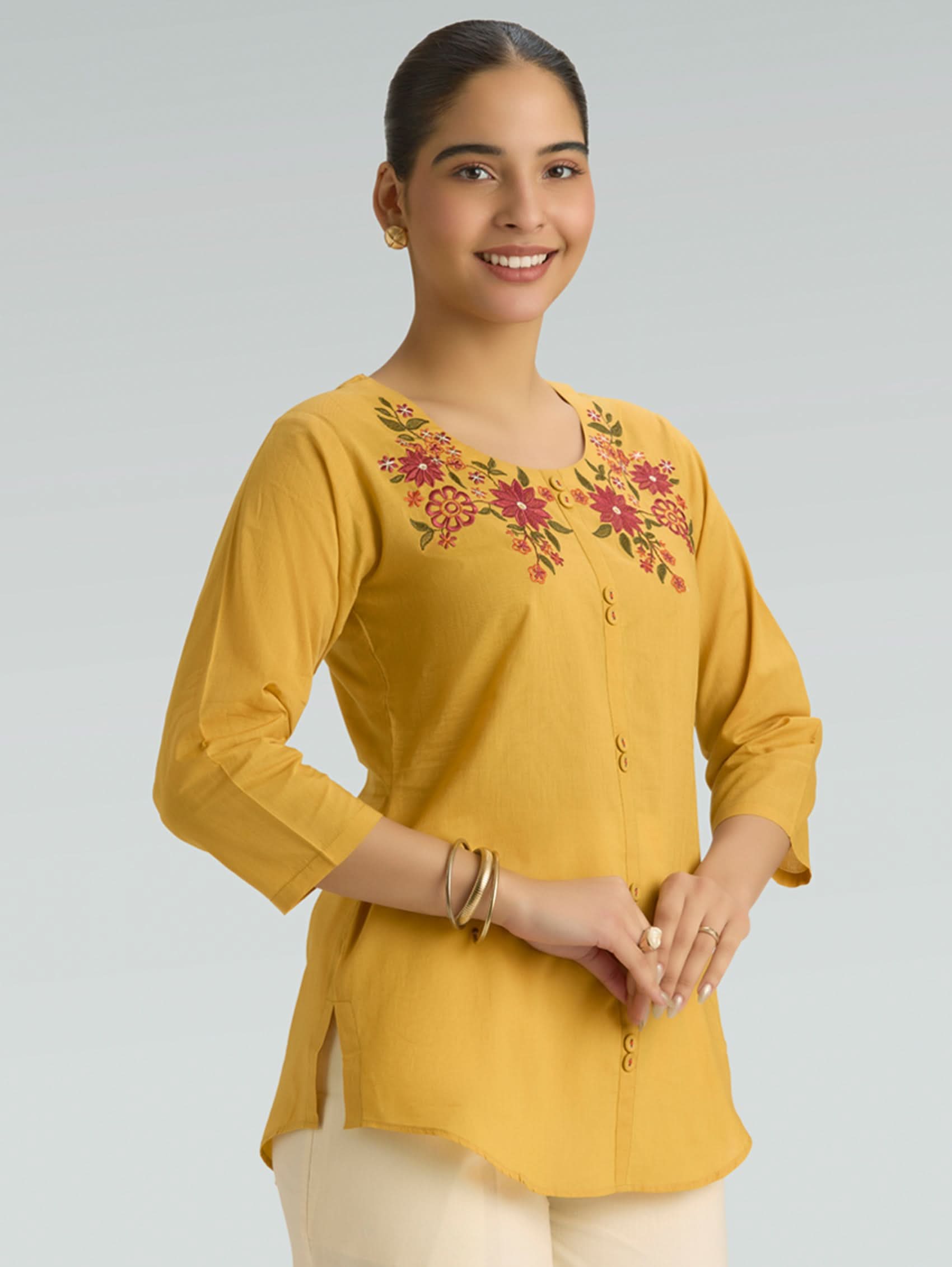 Woman wearing a yellow embroidered top against a gray background