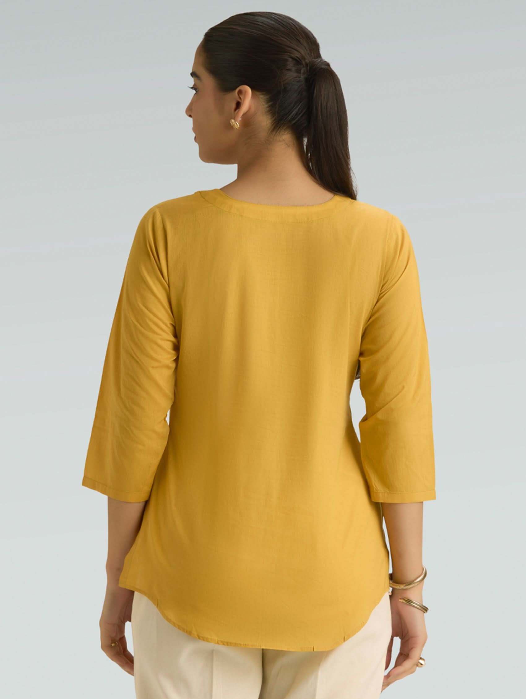 Woman wearing a mustard yellow top against a gray background