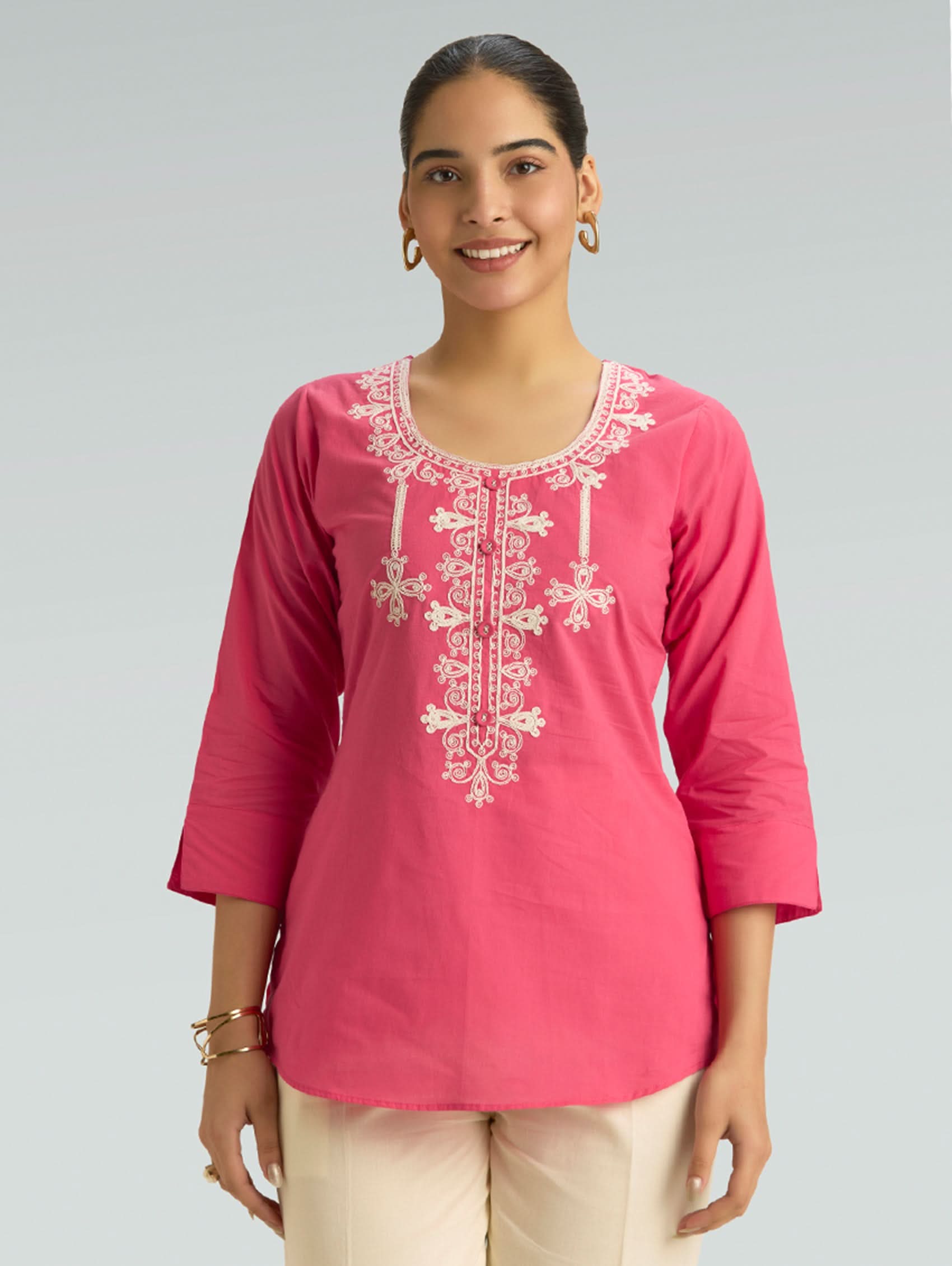 Woman wearing a pink embroidered top against a gray background