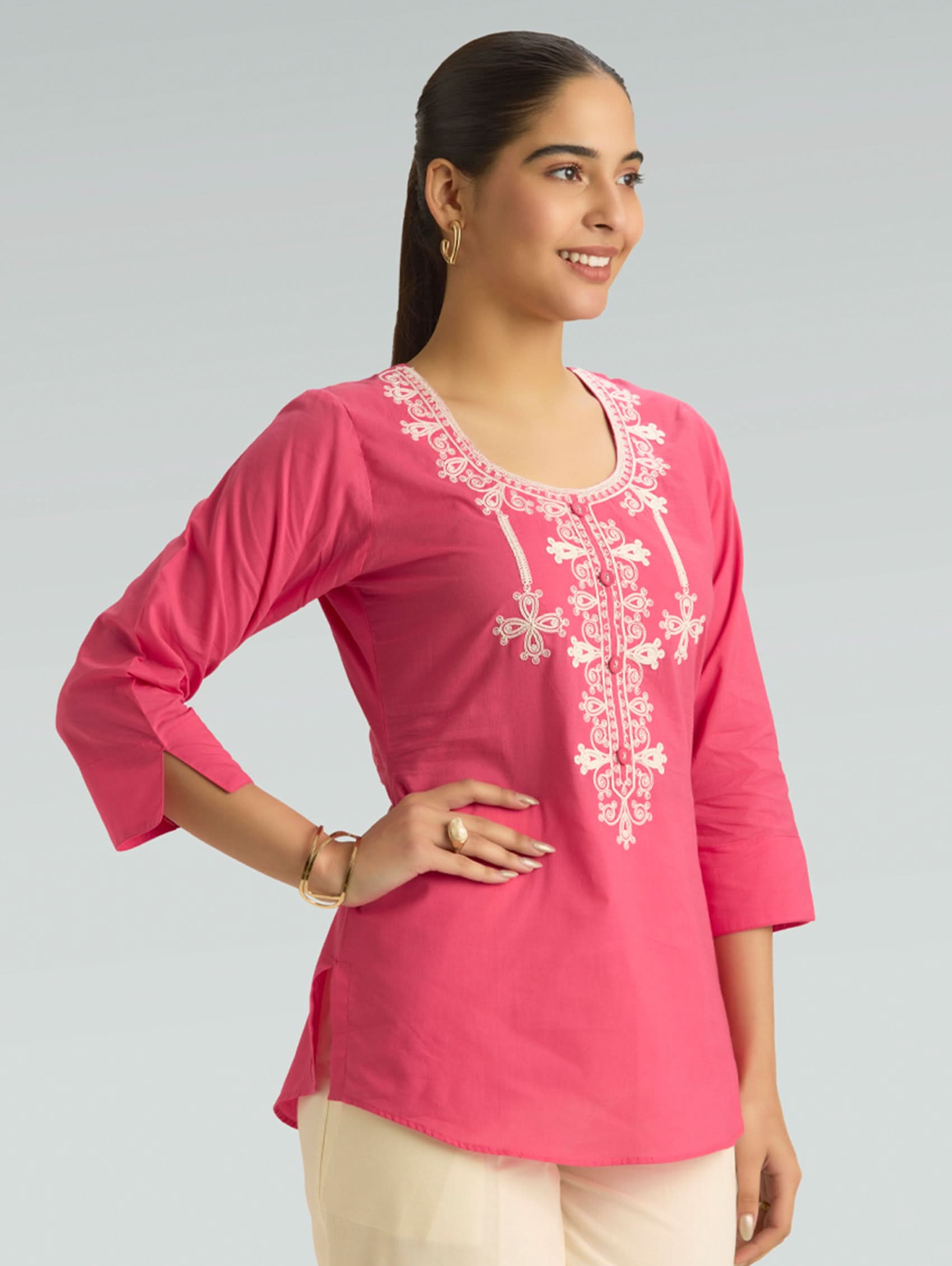 Woman wearing a pink embroidered top on a gray background