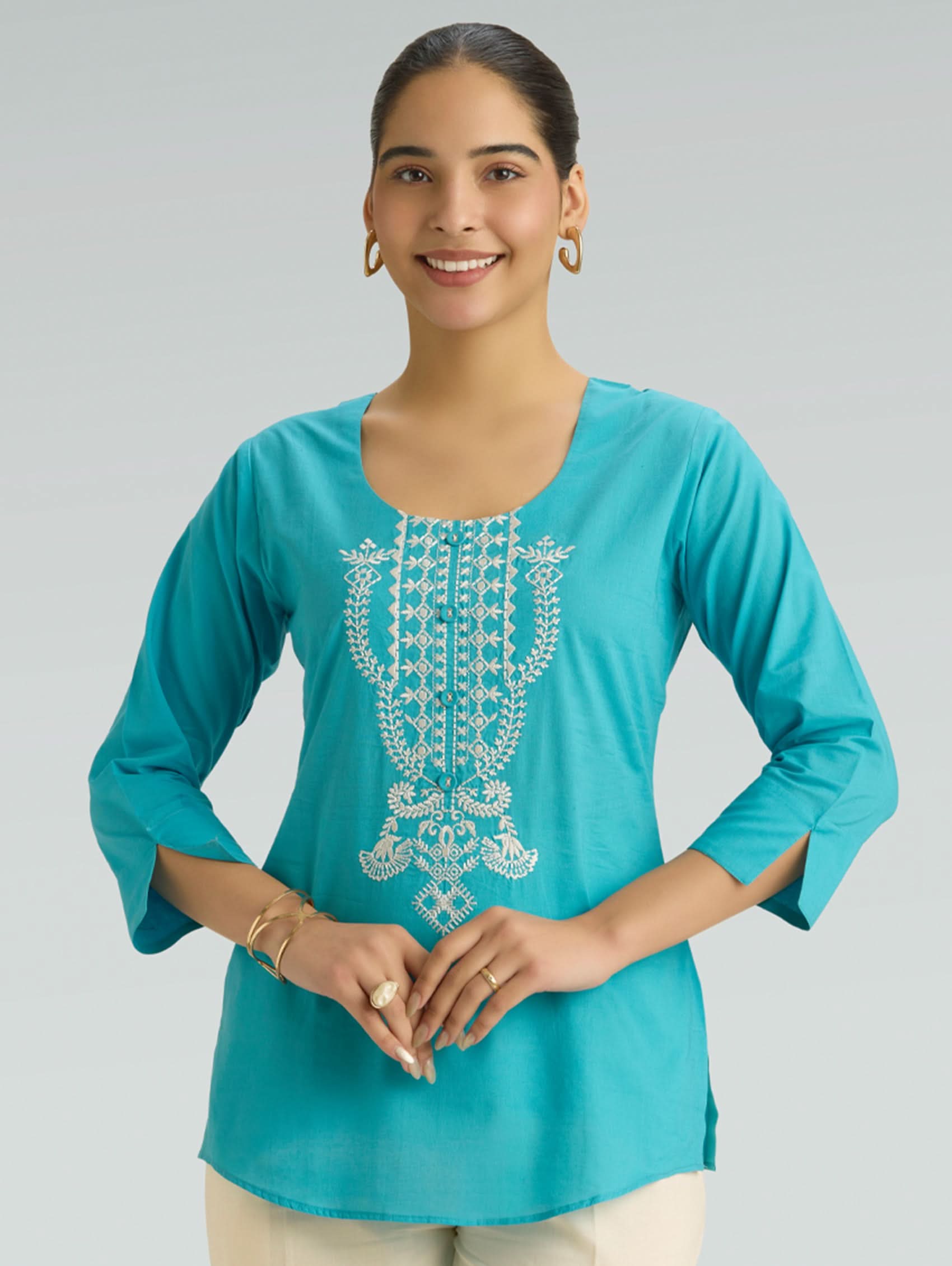 Woman wearing a turquoise embroidered top on a gray background