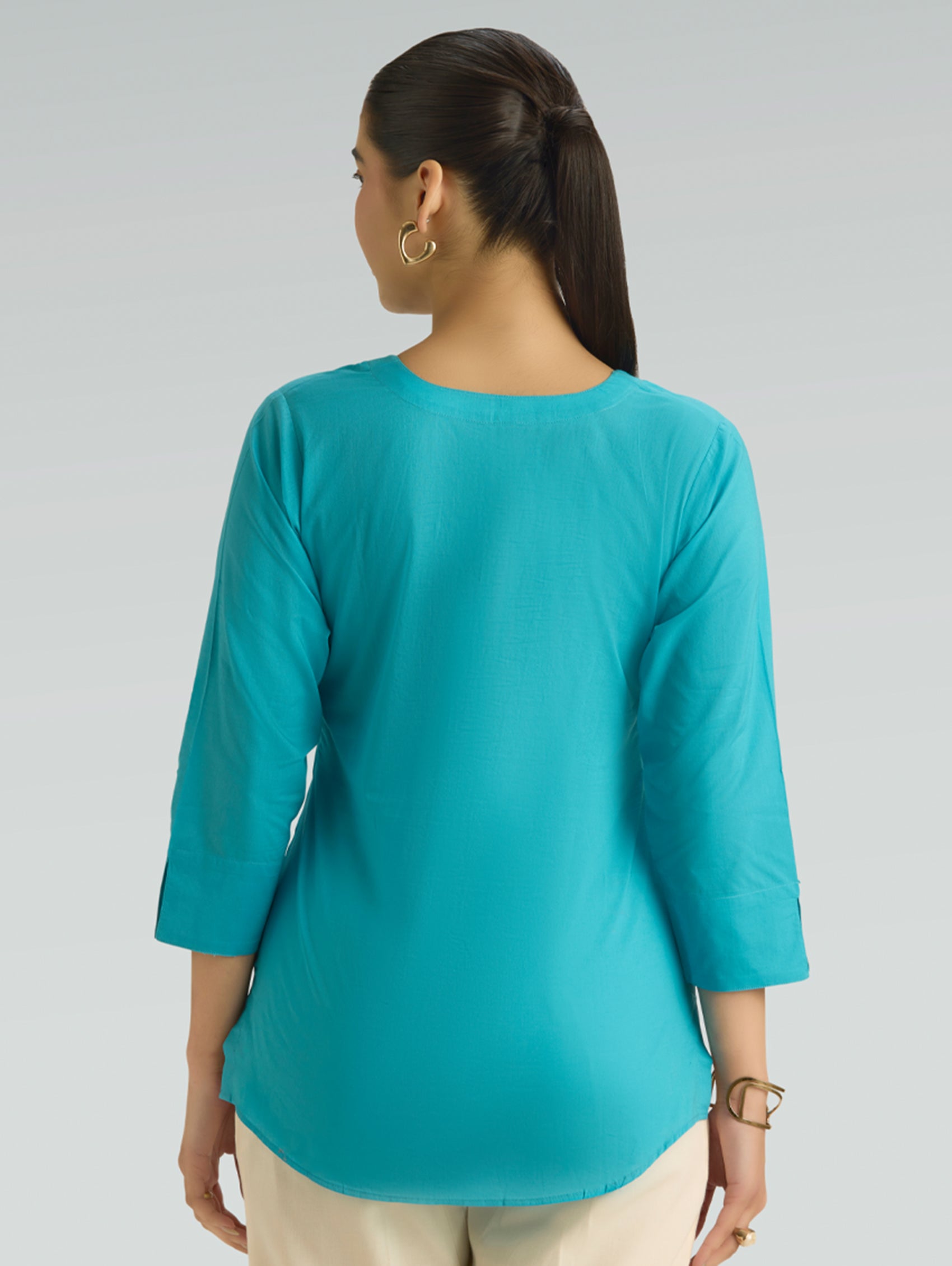 Woman wearing a teal top with three-quarter sleeves on a gray background