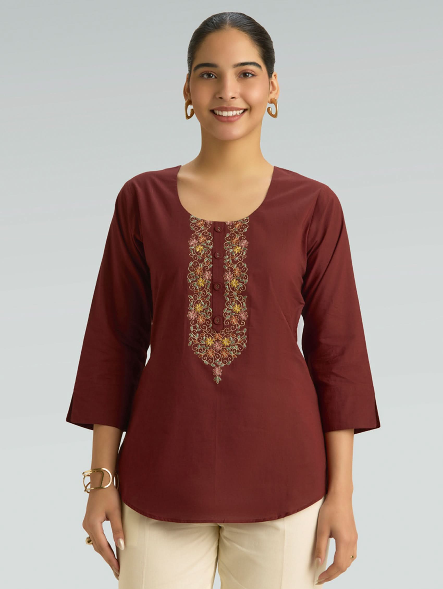 Woman wearing a maroon embroidered top against a plain background