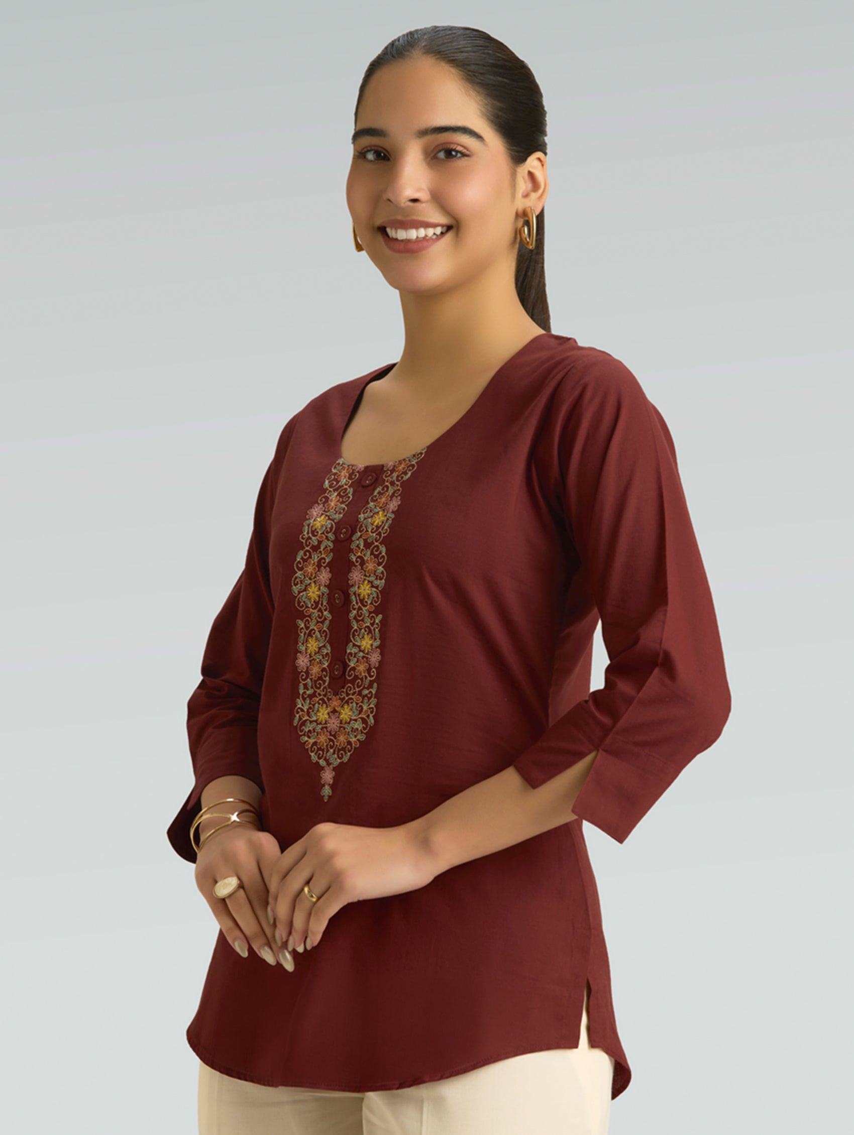 Woman wearing a burgundy top with floral embroidery on a plain background