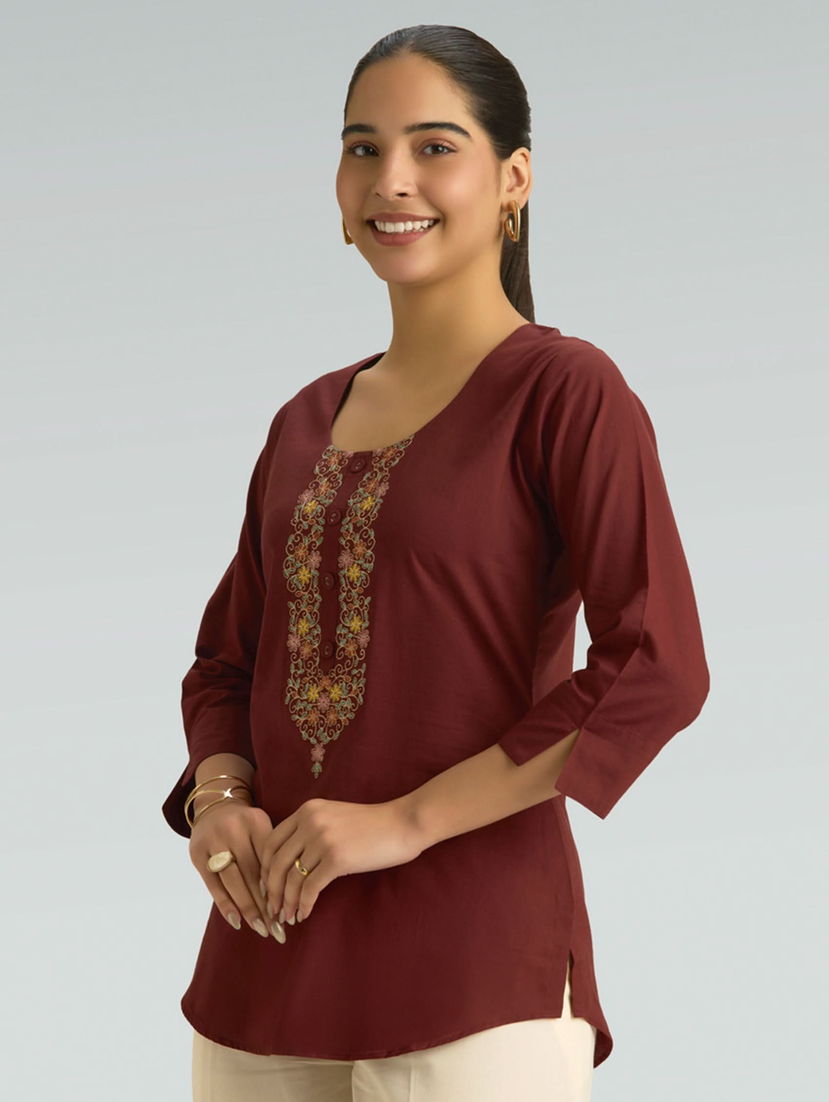 Woman wearing a burgundy top with floral embroidery on a plain background