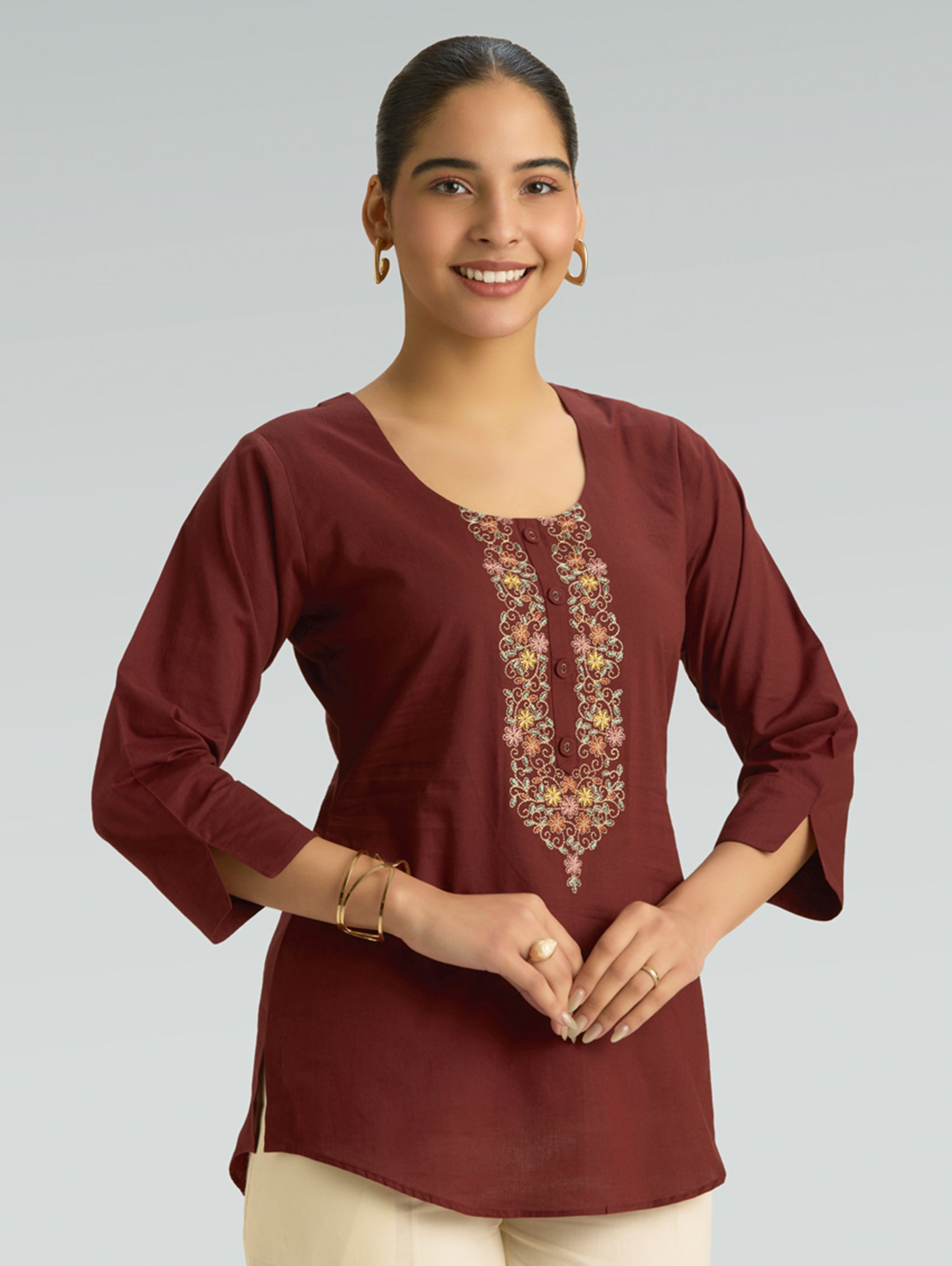 Woman wearing a maroon top with floral embroidery on a plain background