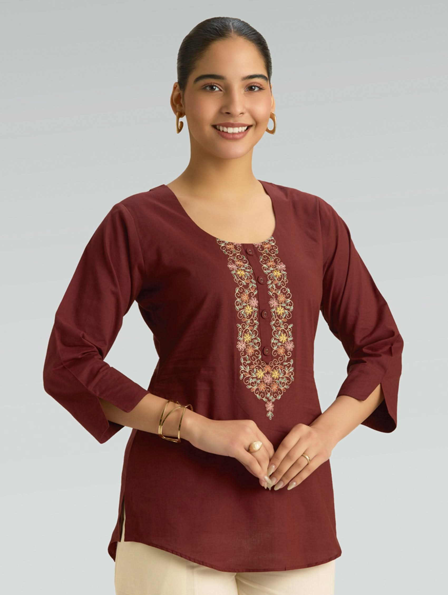 Woman wearing a maroon top with floral embroidery on a plain background