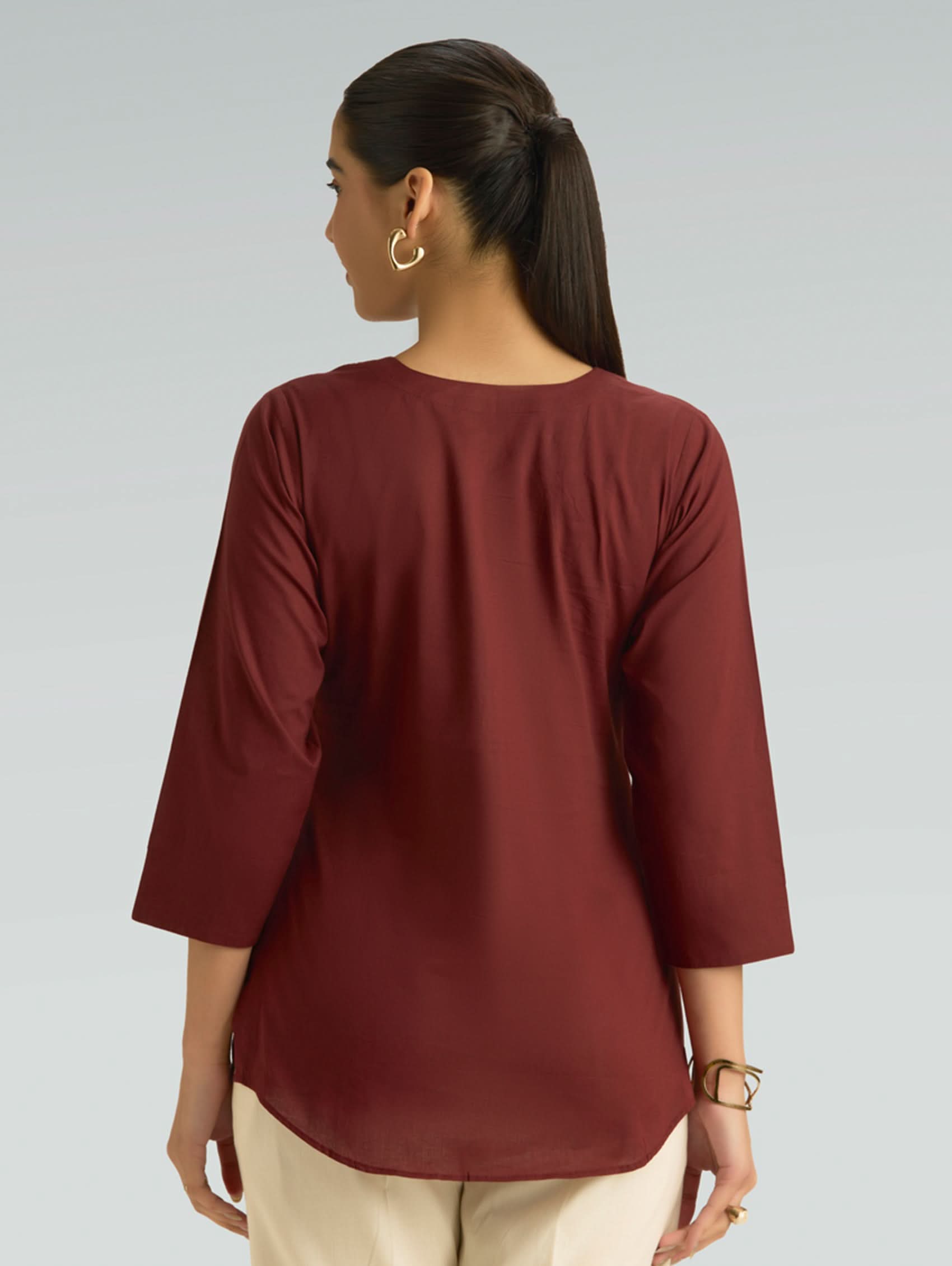 Woman wearing a maroon top with a plain background