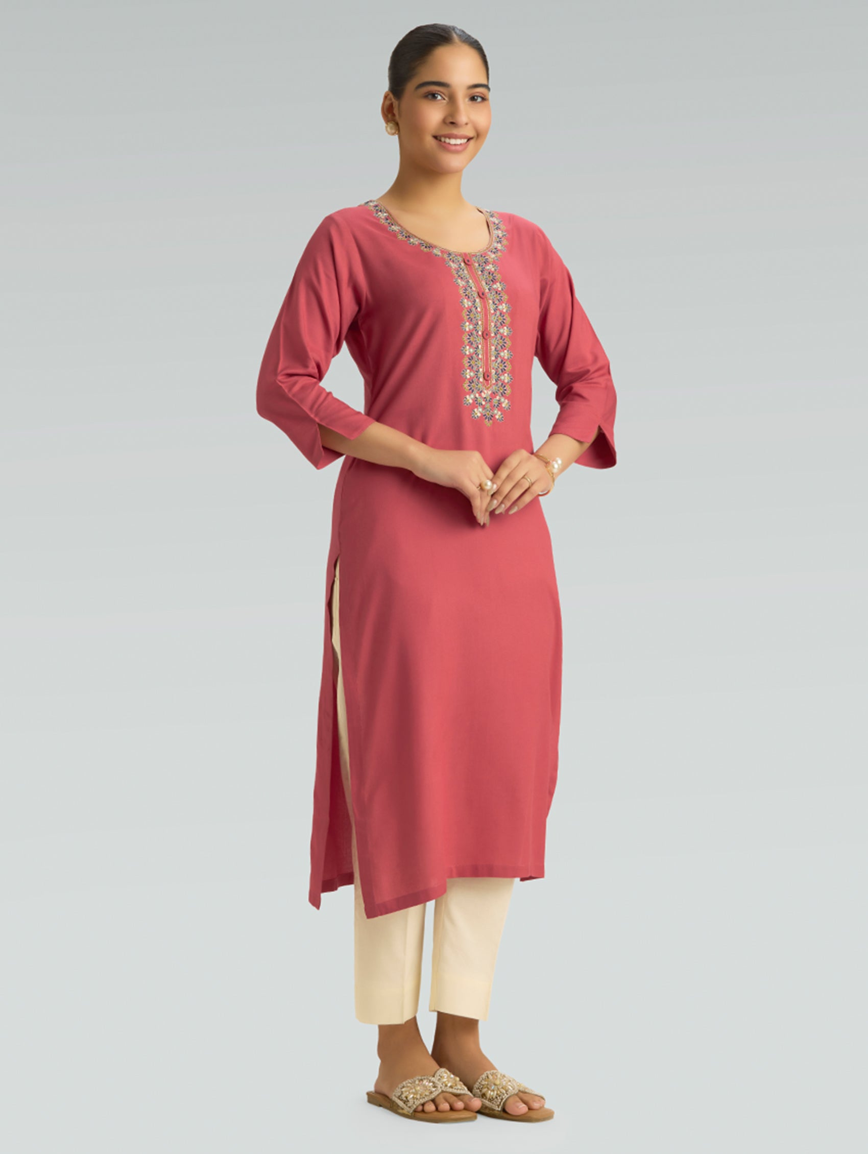 Woman wearing a pink kurta with white embroidery on a gray background