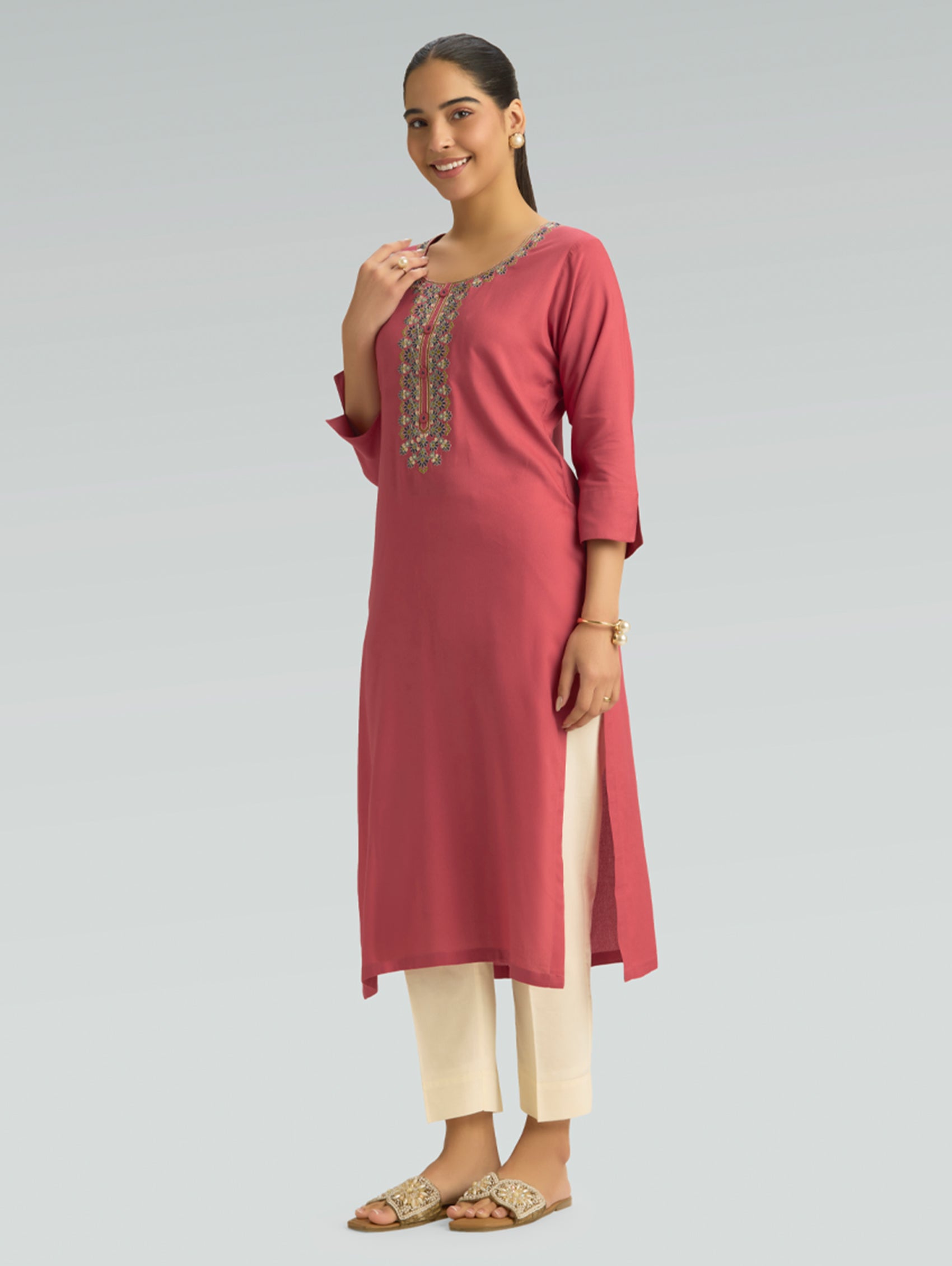 Woman wearing a pink kurta with white pants on a gray background