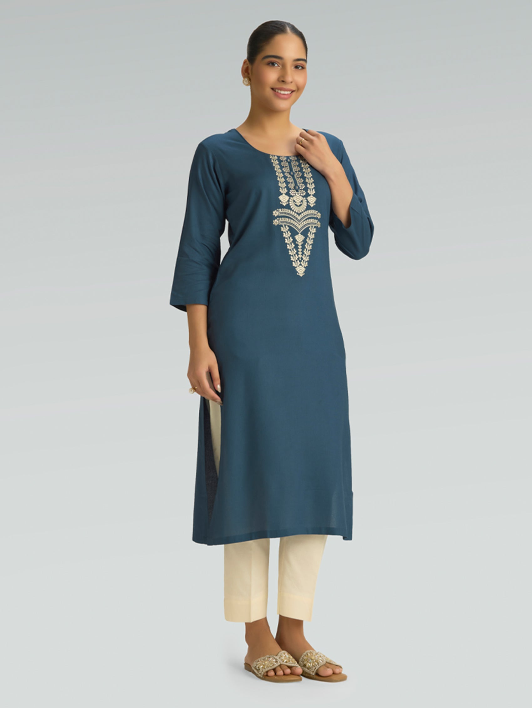 Woman wearing a blue embroidered kurta with white pants on a gray background