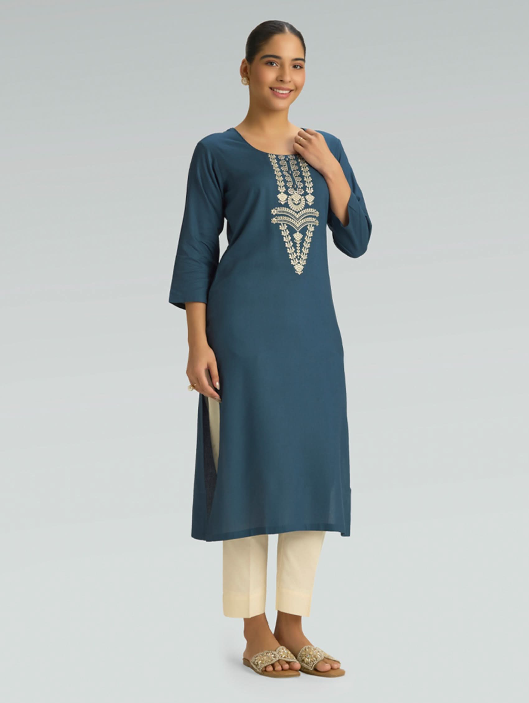 Woman wearing a blue embroidered kurta with white pants on a gray background