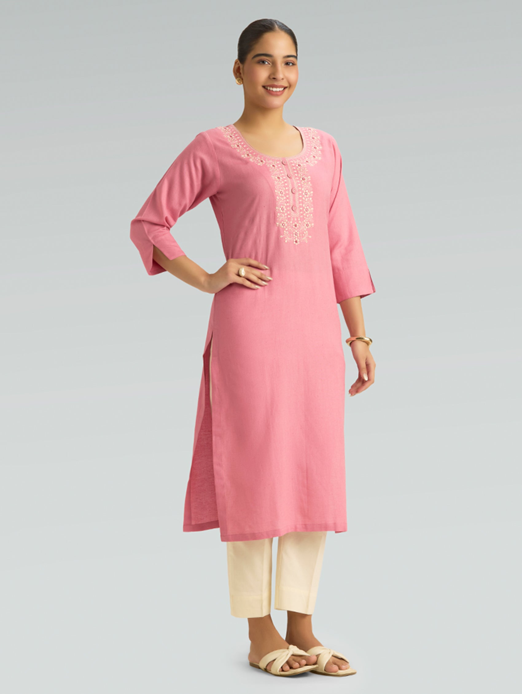 Woman wearing a pink kurta with white embroidery on a gray background