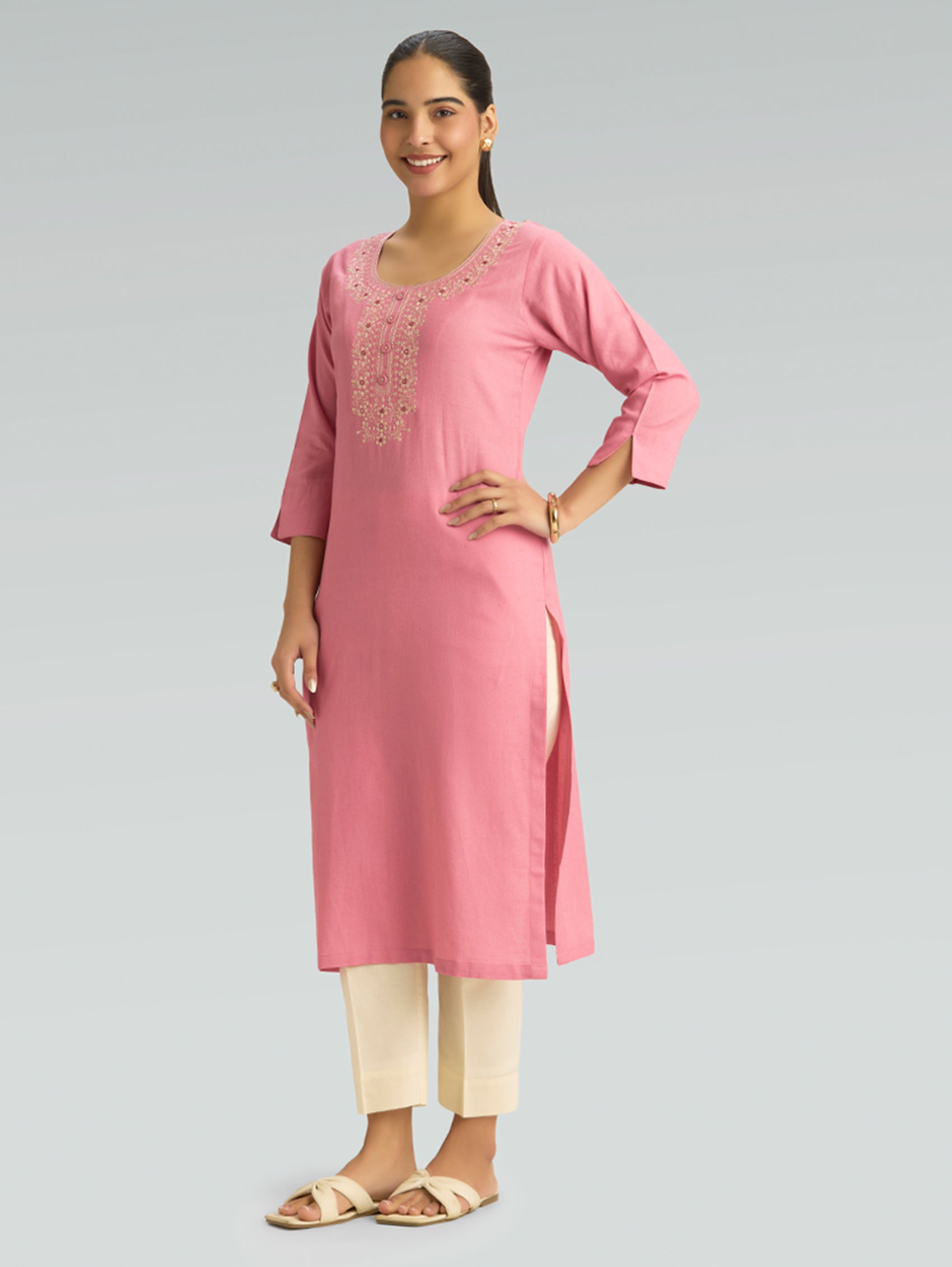 Woman wearing a pink kurta with white pants on a gray background