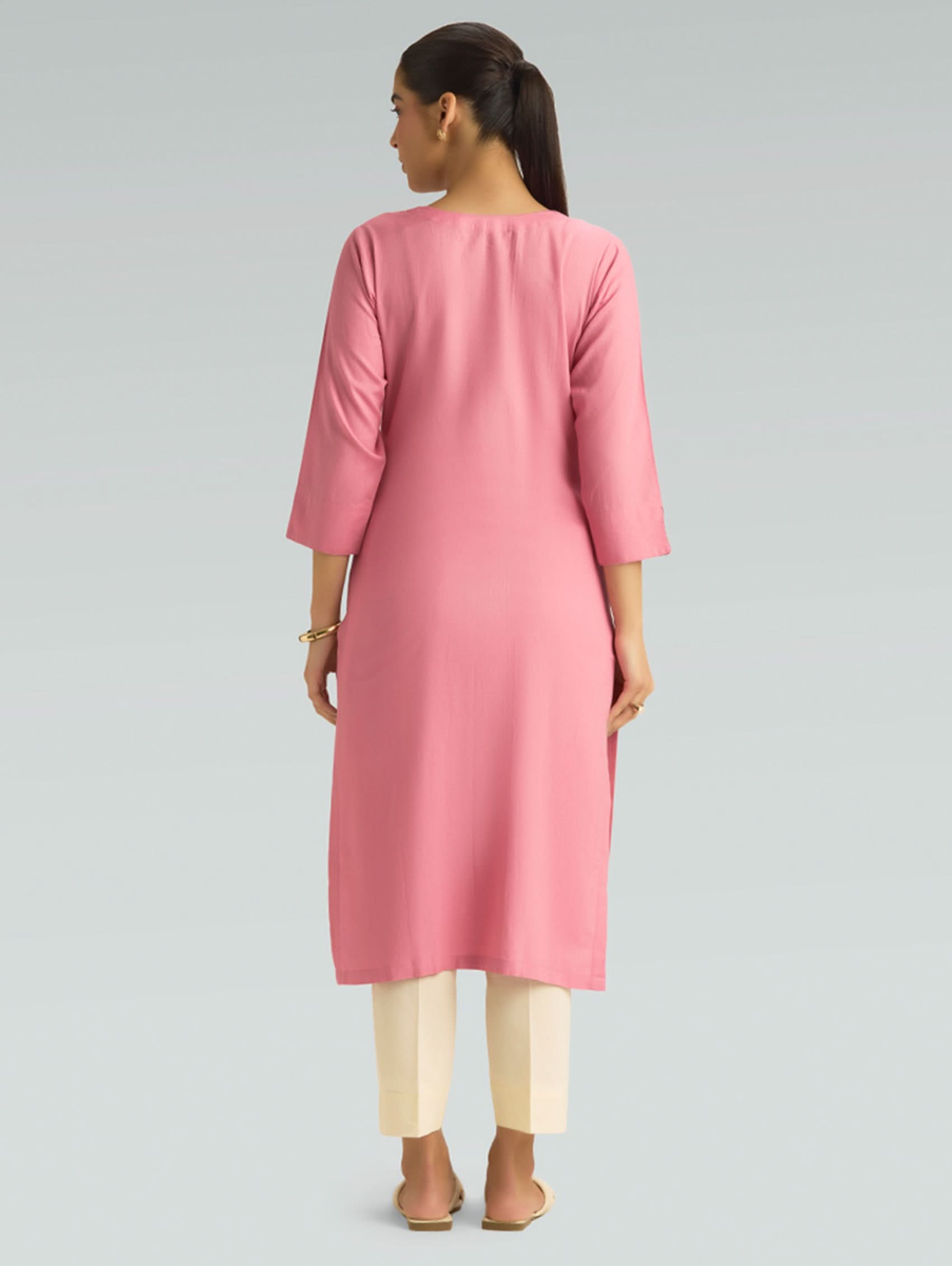 “A woman dressed in a pink kurta paired with white pants, captured in a graceful back pose on a light gray background.”