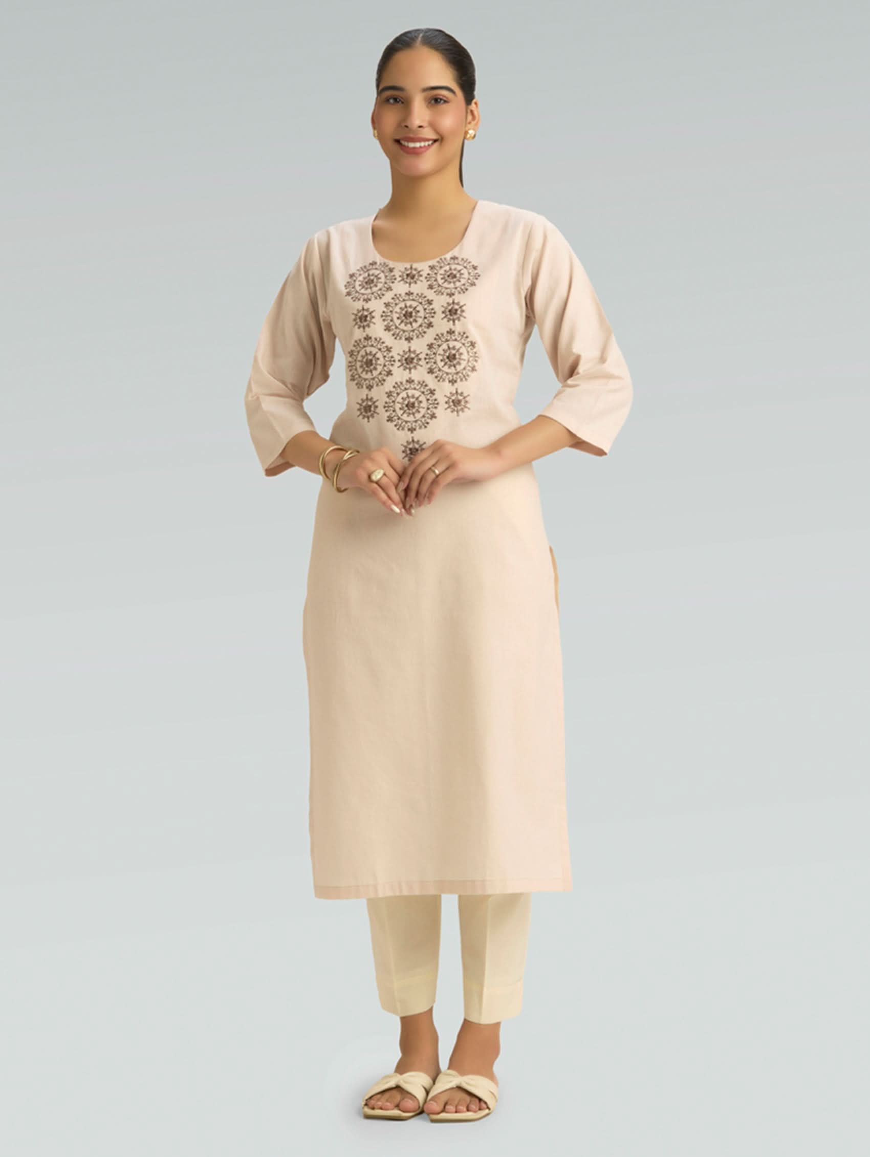 Woman wearing a beige kurta with floral embroidery on a light gray background