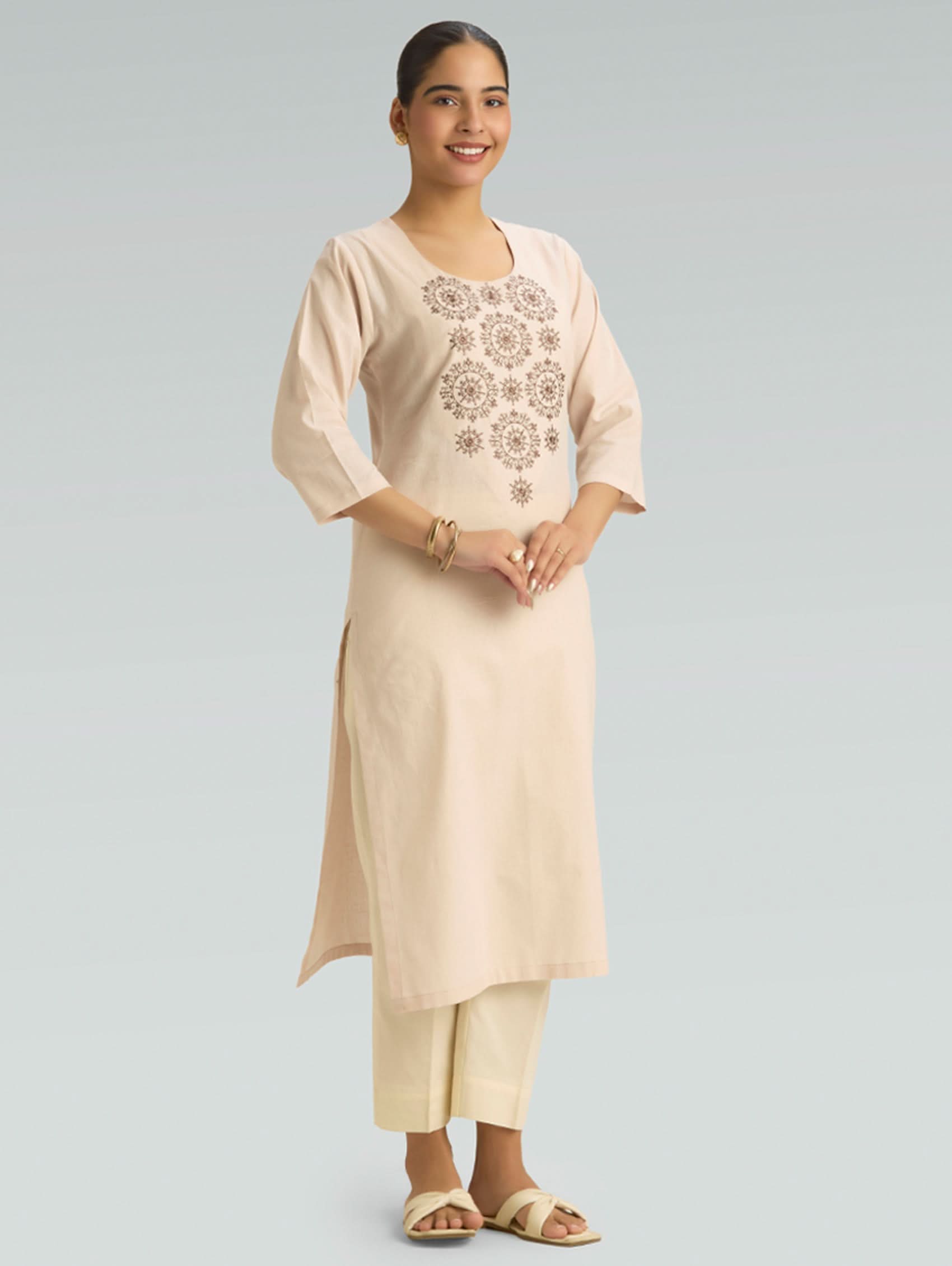 Woman wearing a beige kurta with floral embroidery on a light gray background