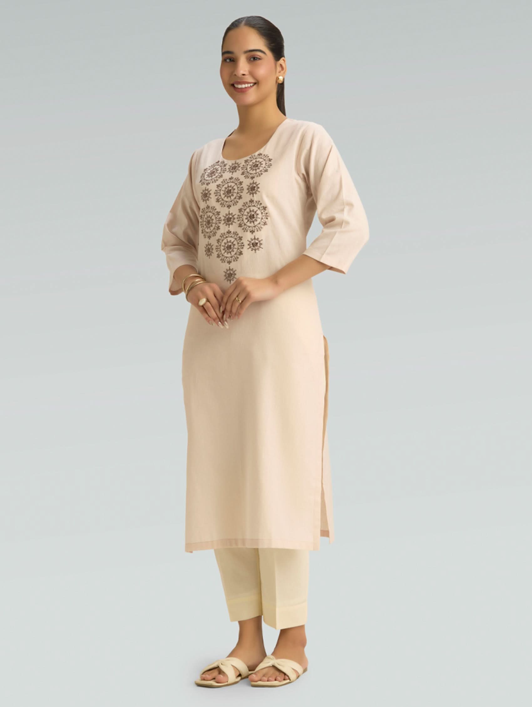 Woman wearing a beige kurta with an embroidered top and matching pants on a light gray background