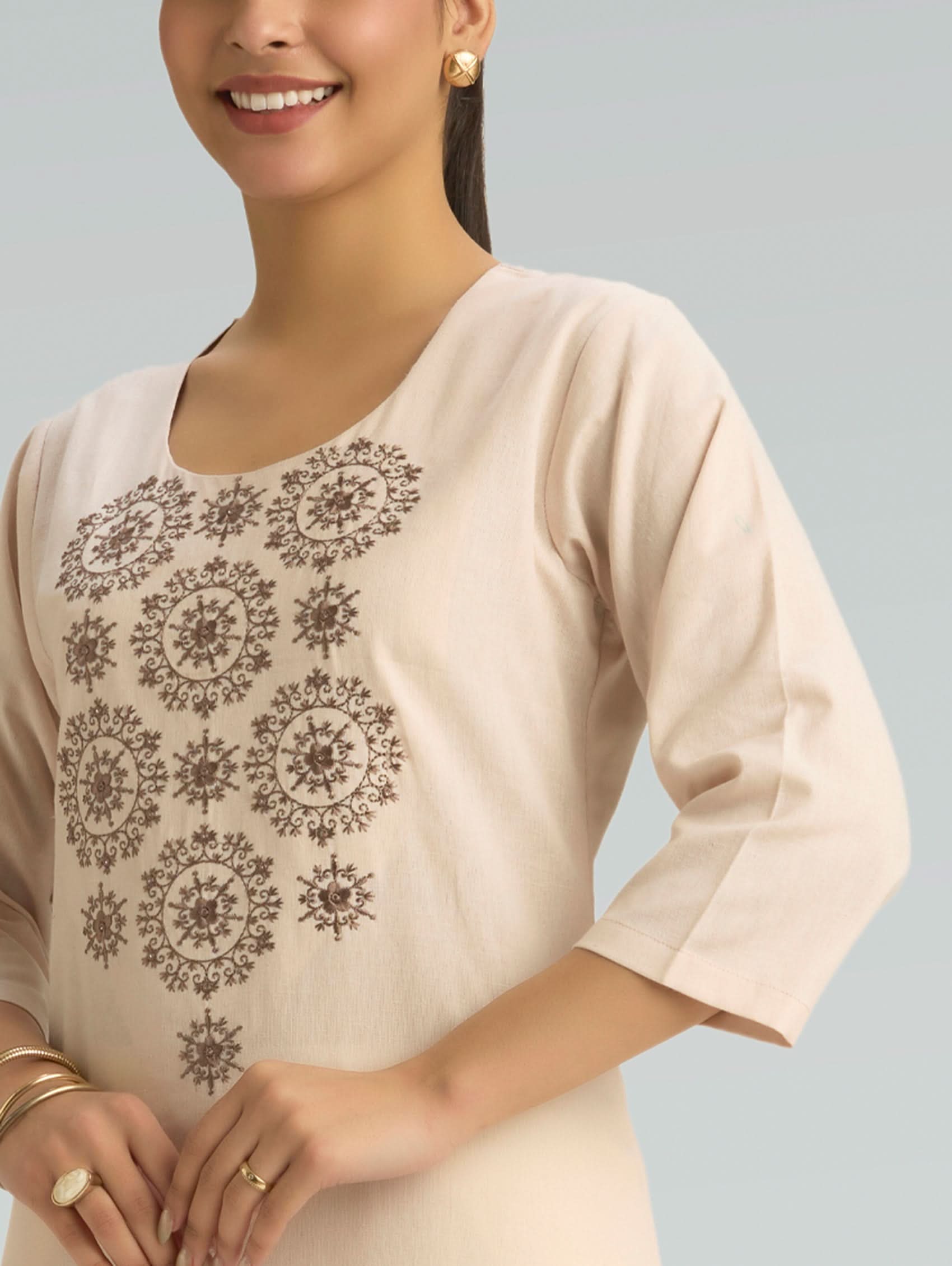 Woman wearing a beige top with intricate black patterns on a light gray background