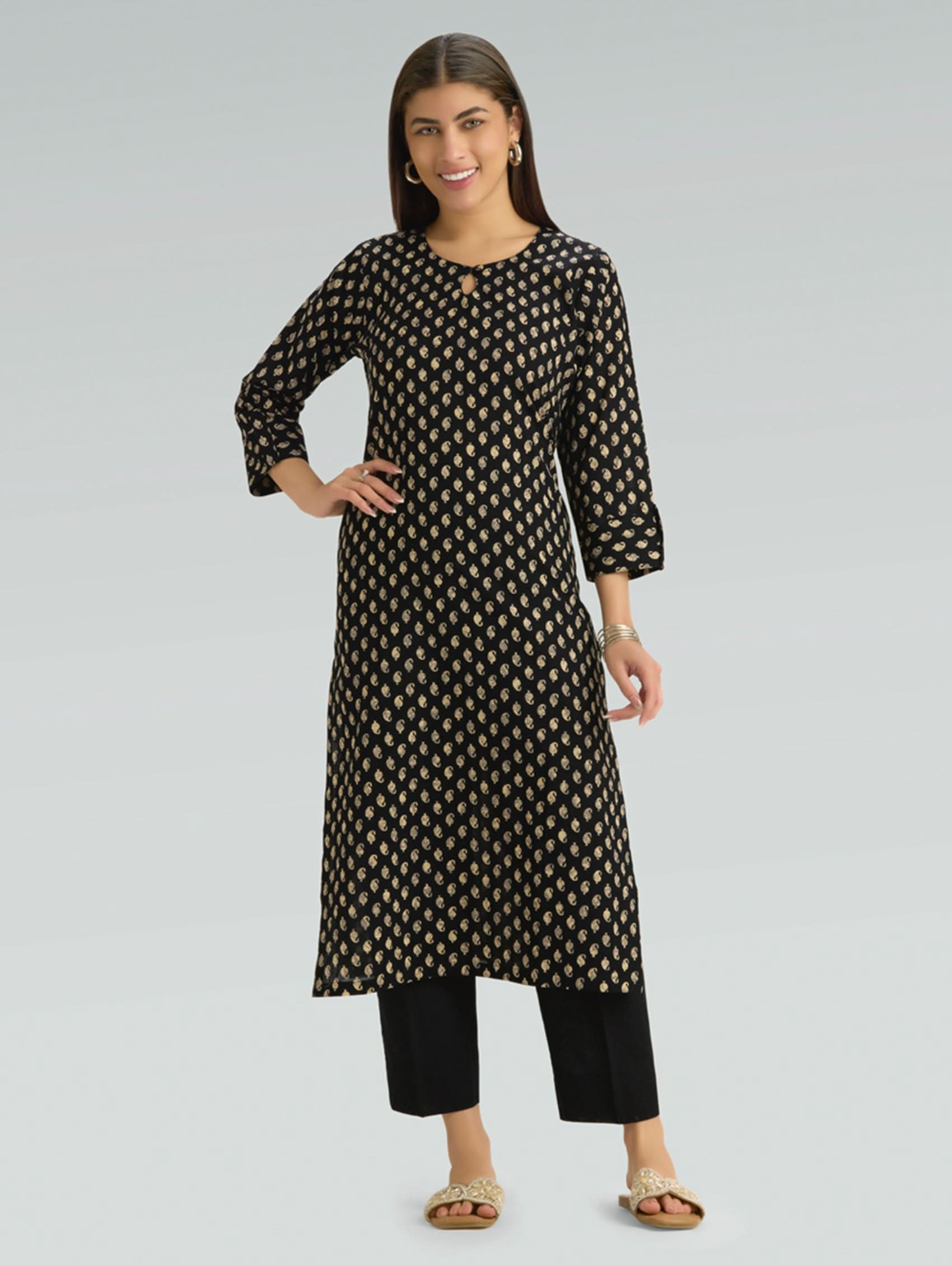 Woman wearing a black and gold patterned kurta with black pants on a light gray background