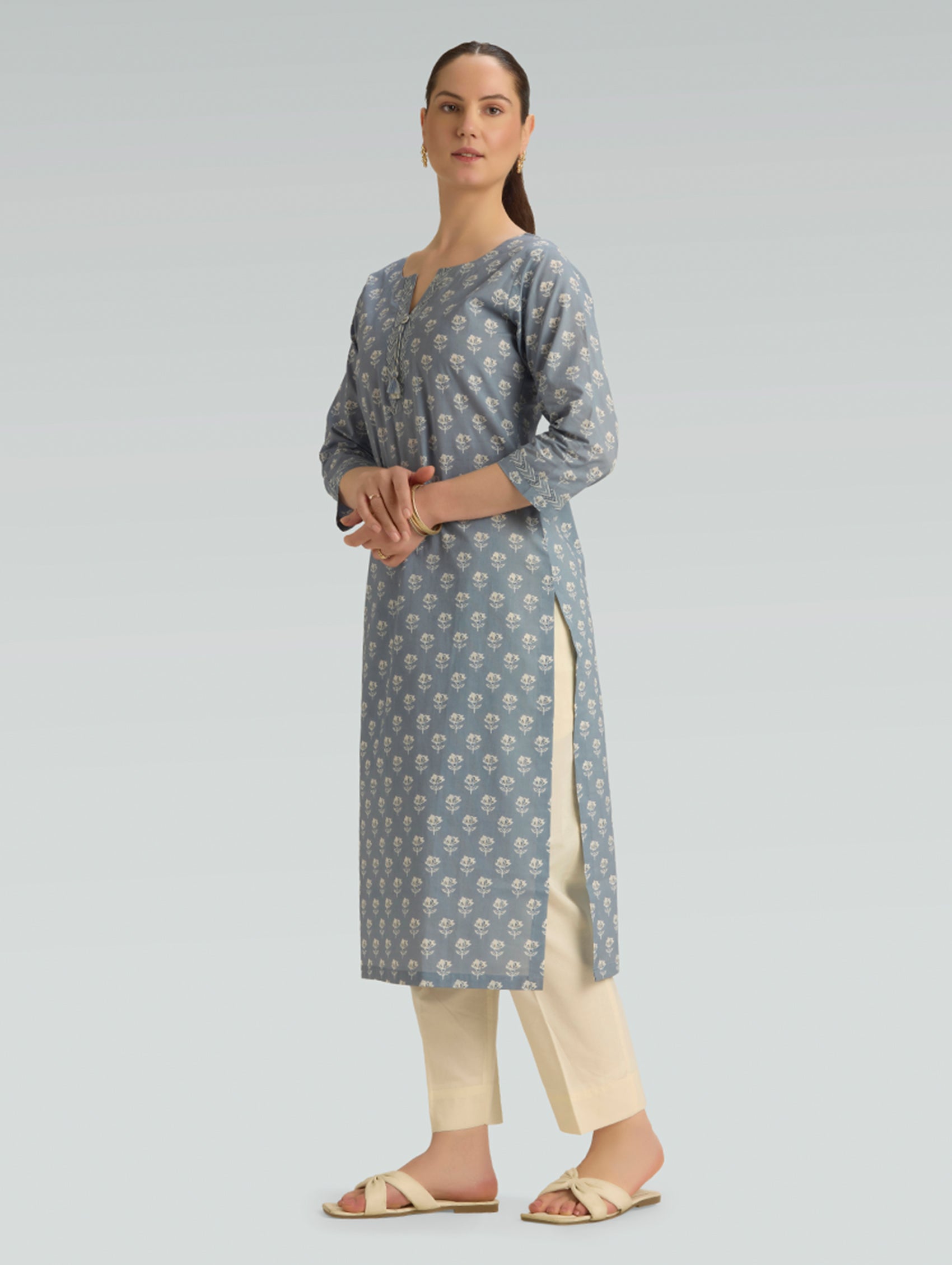 Woman wearing a gray floral patterned kurta with beige pants on a light gray background
