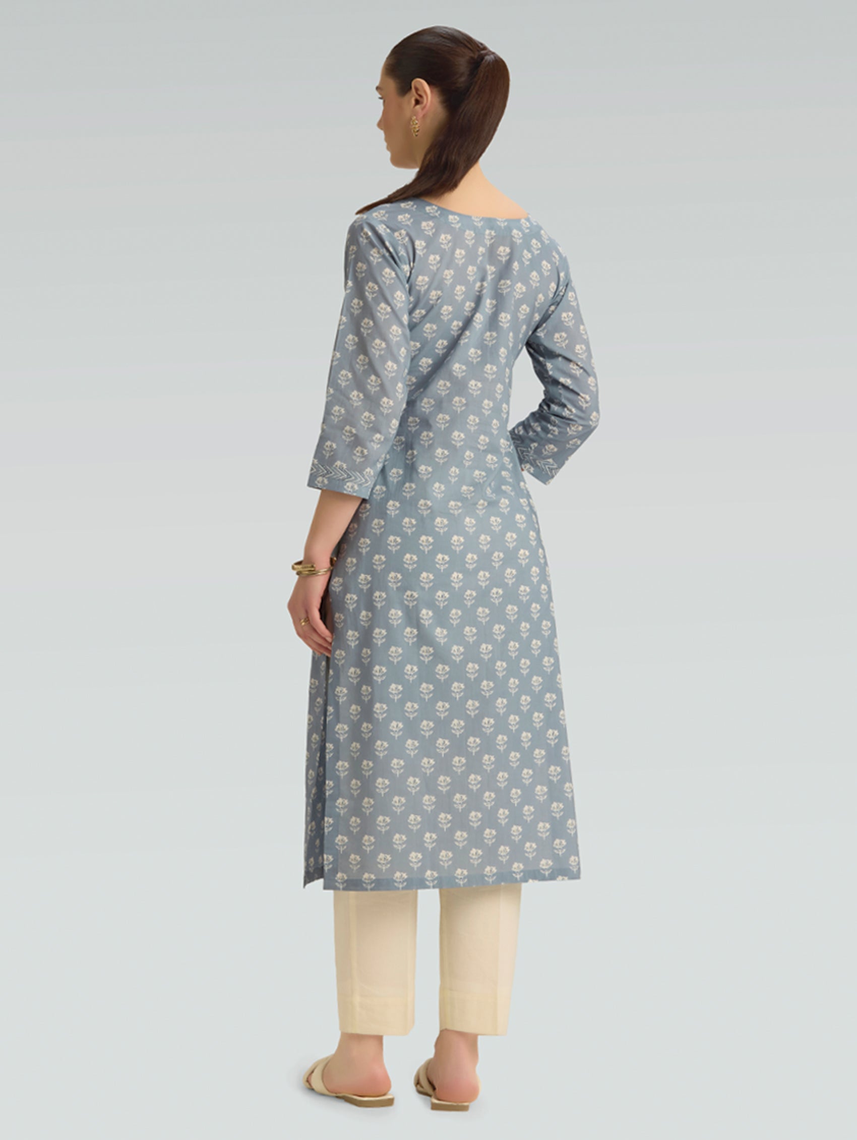 “A woman dressed in a gray patterned kurta paired with beige pants, captured in a graceful back pose on a light gray background.”