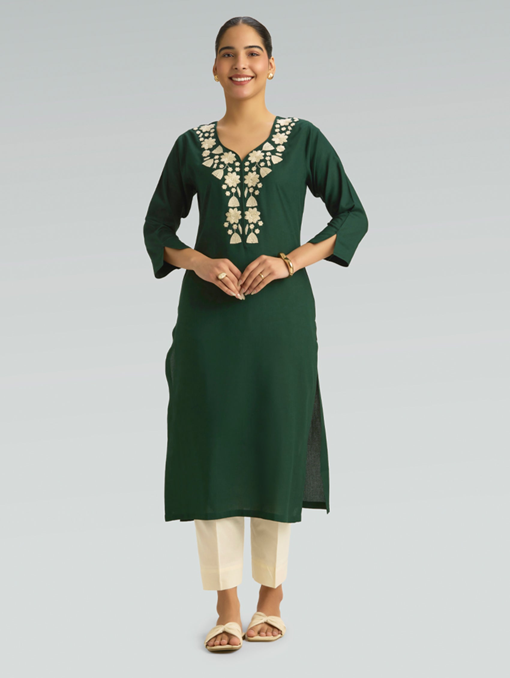 “A woman wearing a straight-fit green kurta with a round neckline and computerized thread embroidery, set against a gray background.”